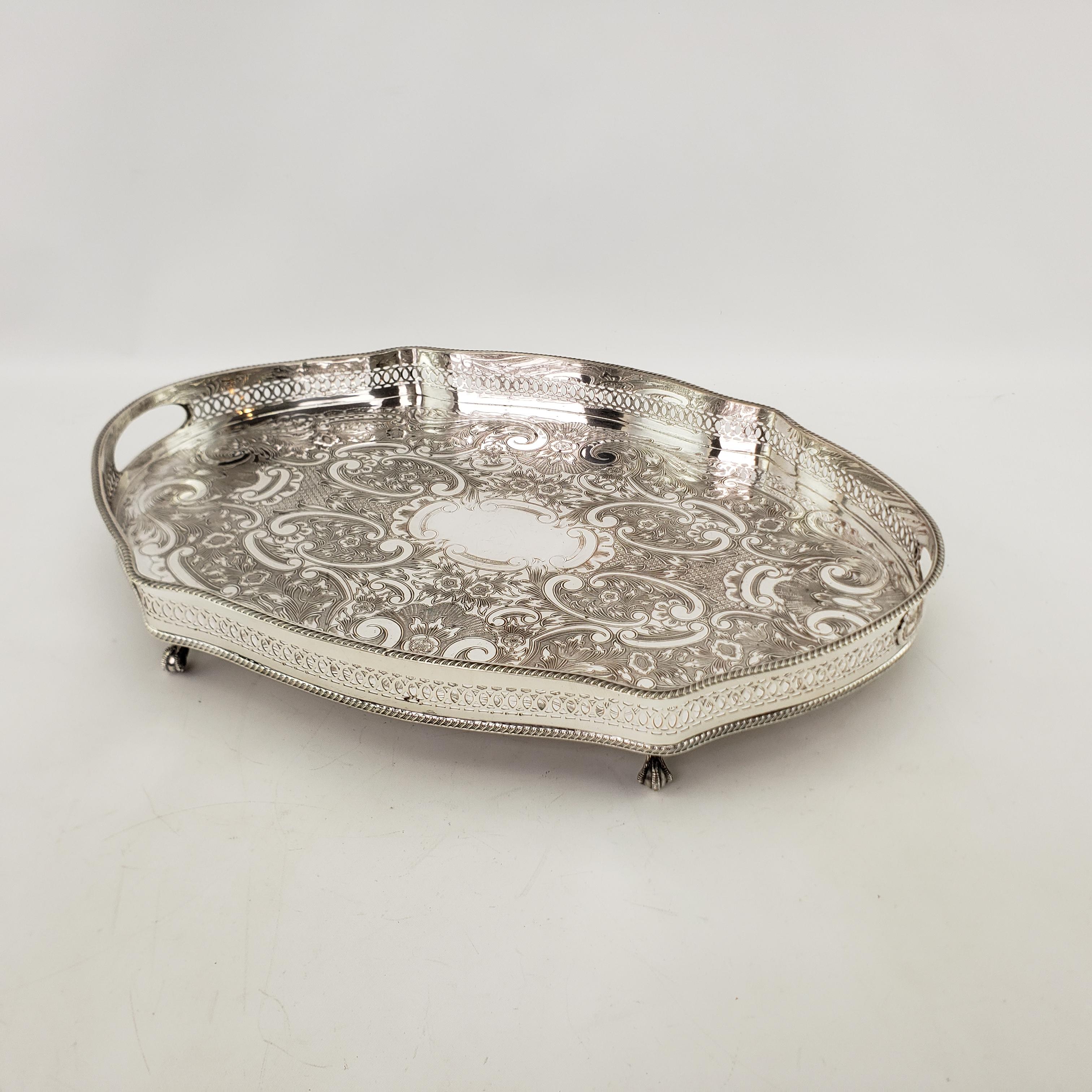 This antique gallery serving tray was made by APEX of England in approximately 1920 in a Victorian style. The tray is composed of silver plate with a serpentine shape and ornate engraving on the surface. The handles are inset within the gallery and