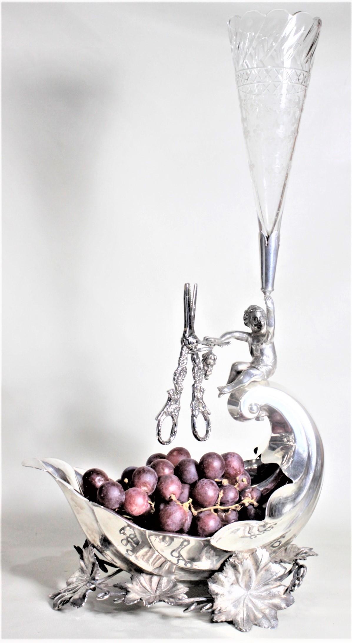 This. antique silver plated figural centerpiece is unsigned, but presumed to have been made in England in circa 1880 in the period Victorian style. The centerpiece features a figural child grape stand in the center, which overlooks a large scalloped