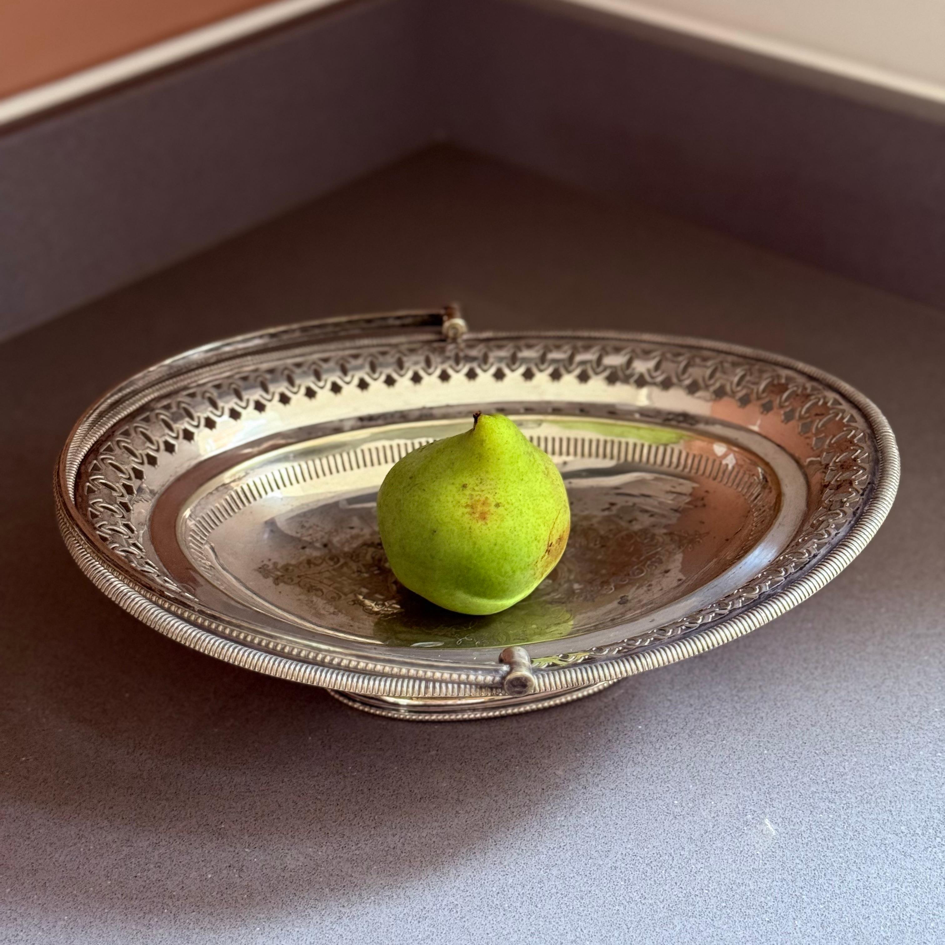 Un cesto di frutta antico placcato in argento di ottima fattura, caratterizzato da un elegante bordo traforato a galleria e da un manico oscillante a corda finemente dettagliato. La forma ovale poggia saldamente su un piede rialzato, offrendo