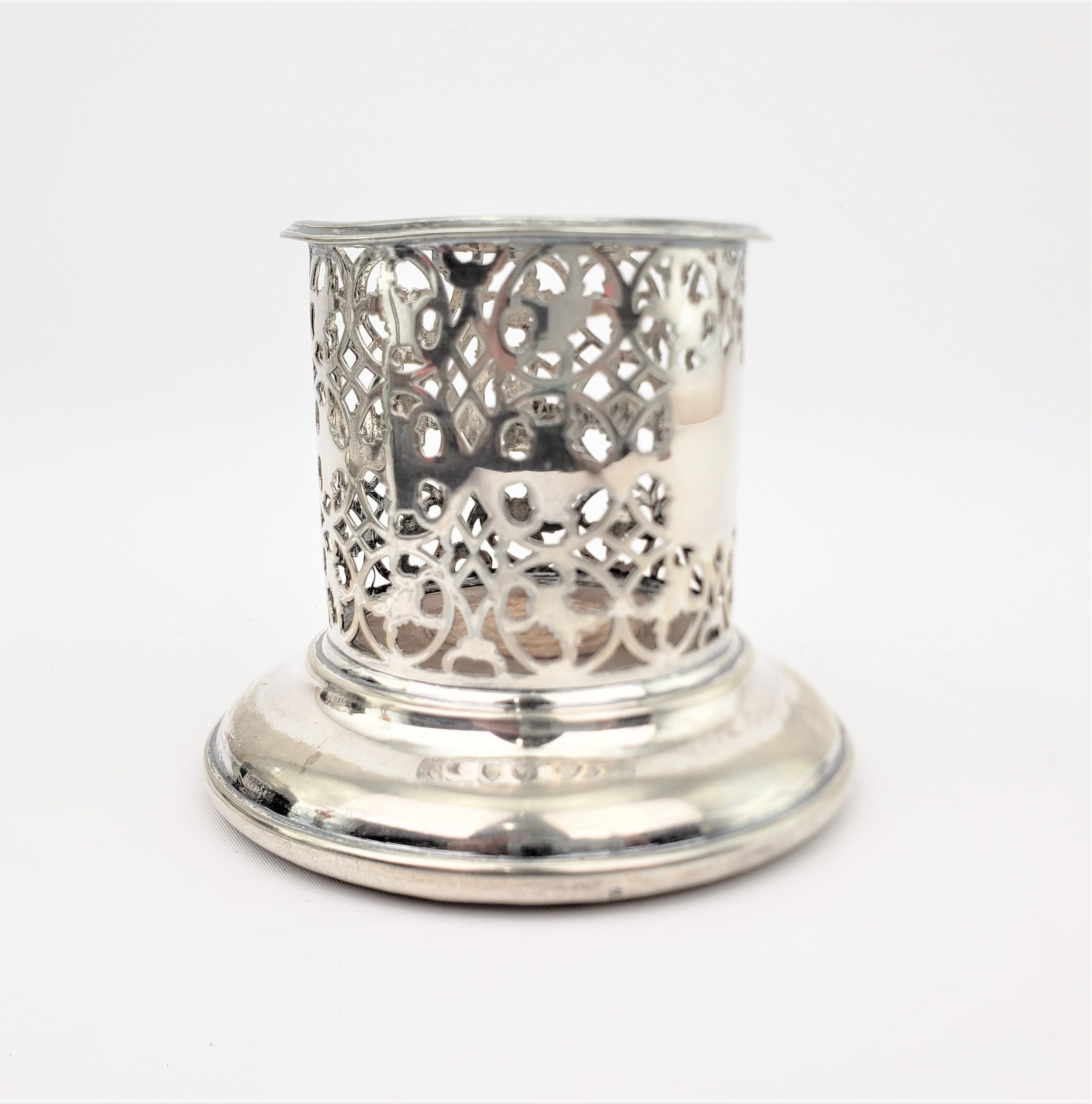 This silver plated bottle coaster is unsigned, but presumed to have been made in England in approximately 1920 in a slightly earlier Edwardian style. The coaster has tall pierced gallery styled sides with a shield medallion on the front which has