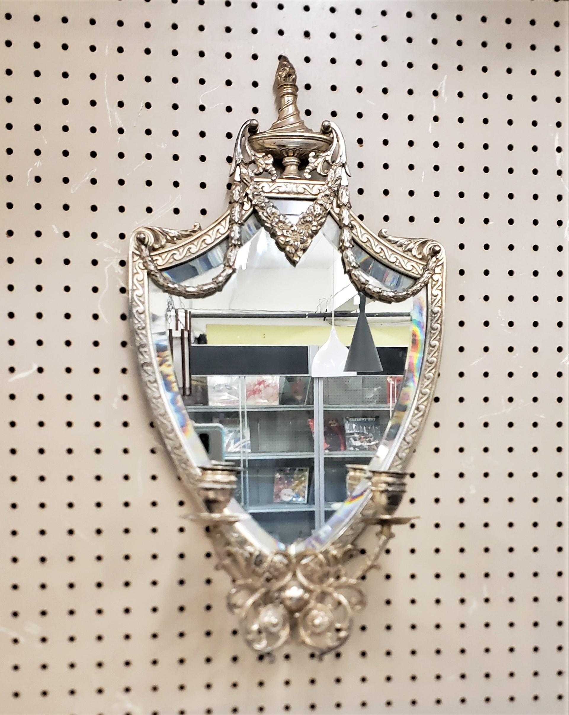 This antique silver plated wall mirror or candle sconce is marked by an Unknown maker on the back, but presumed to have been made in the United States in approximately 1900. The beveled wall mirror is shield shaped with raised vine and garland