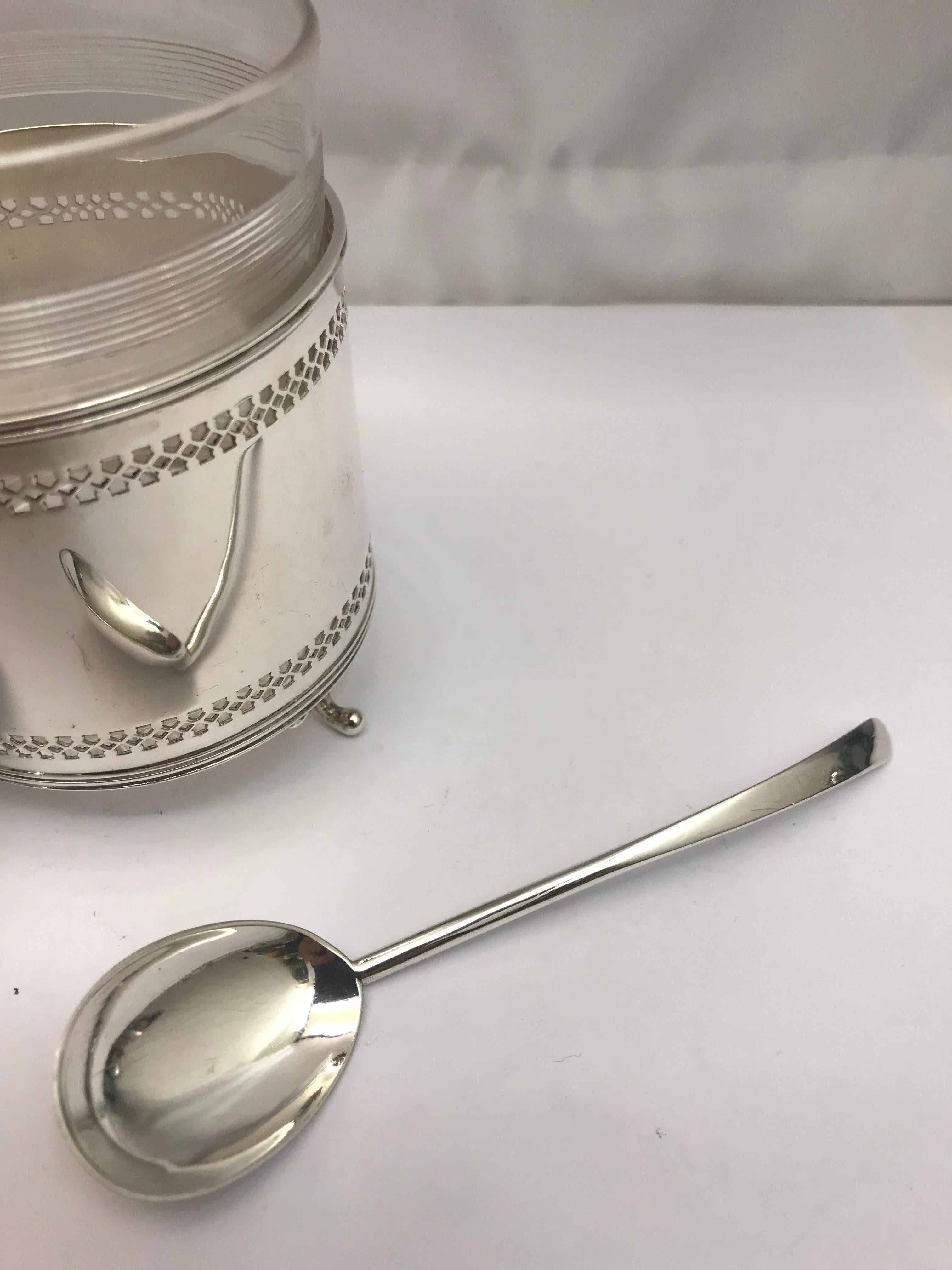 An antique silver and glass pot/mustard pot with cover and spoon. 

Sitting on 3 small silver ball feet.

Made in England, 1919.