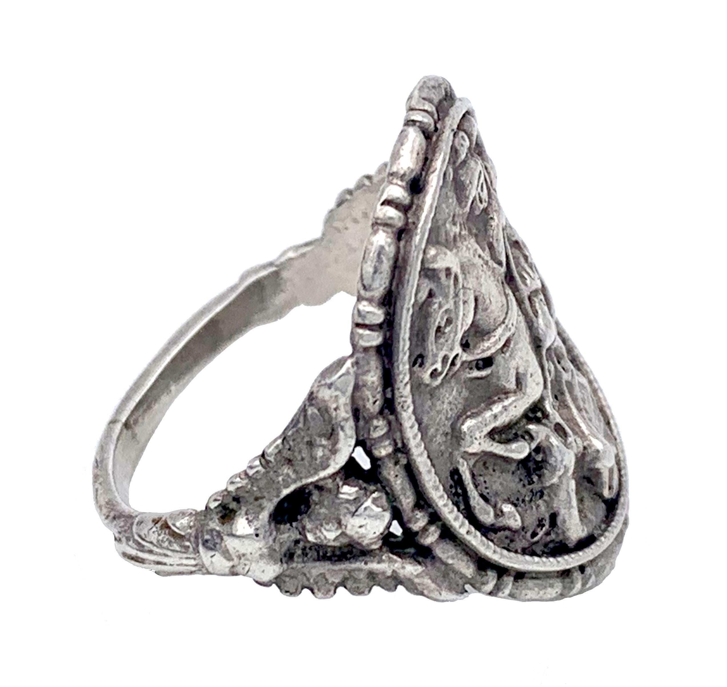 This  antique silver ring shows Saint George fighting the dragon on the curbed ring head  The reverse shows Saint Eustace kneeling in front of a dear.
The ring shoulders are designed as winged caryatids.
Ringsize 54