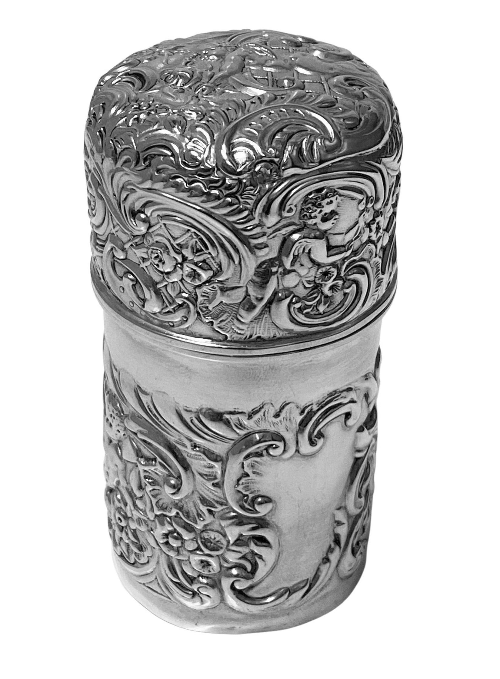 Antique silver scent bottle with removeable glass interior, London 1895 William Comyns. Cylindrical form decorated with putti cherub and angels amidst foliage, vacant cartouche to front. Hinged cover, gilded interior with removeable clear glass