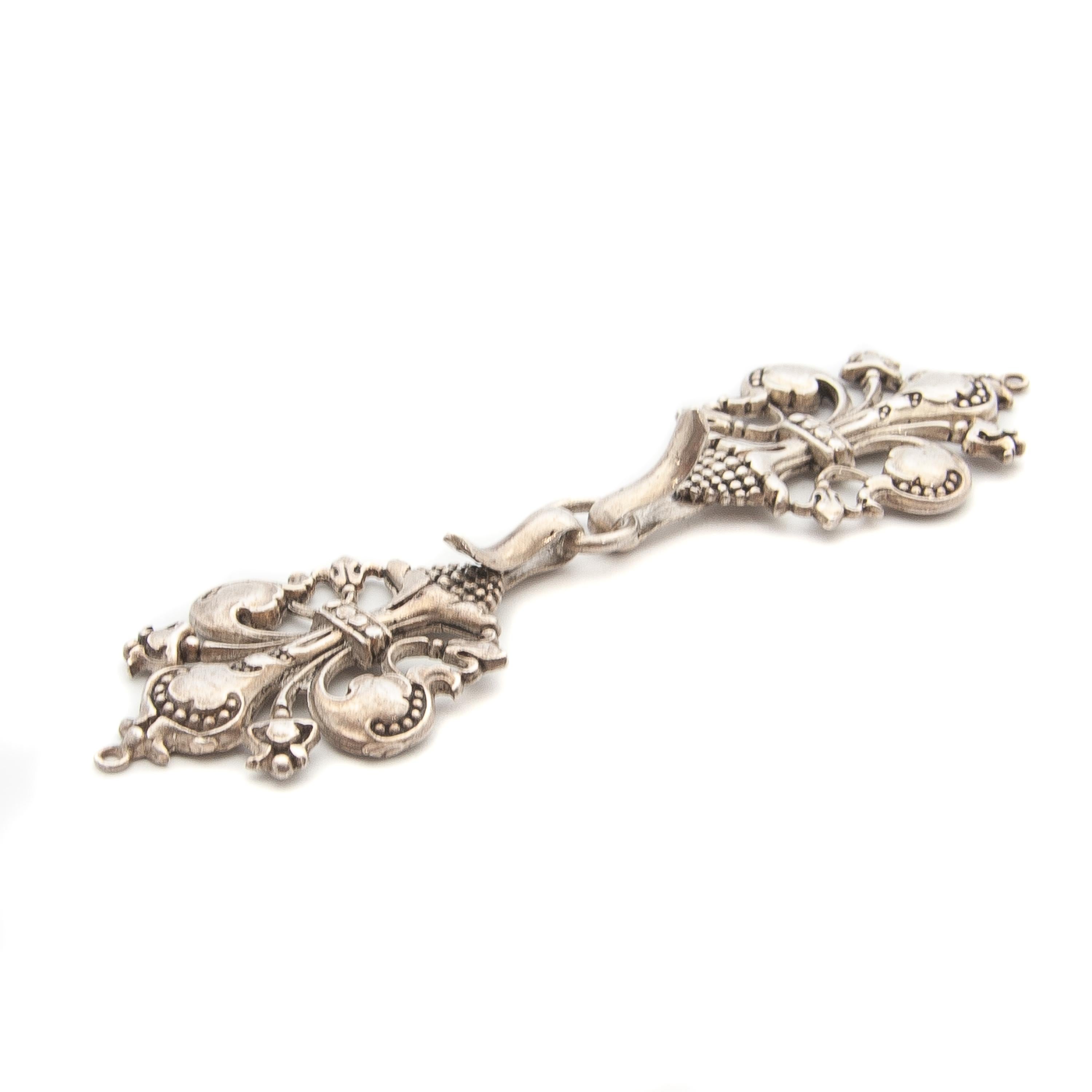 This ornate silver shawl buckle is a beautifully crafted accessory, likely dating from the late 19th to early 20th century. It features an elaborate Rococo or Baroque Revival design, characterized by scrollwork, beaded detailing, and stylized floral