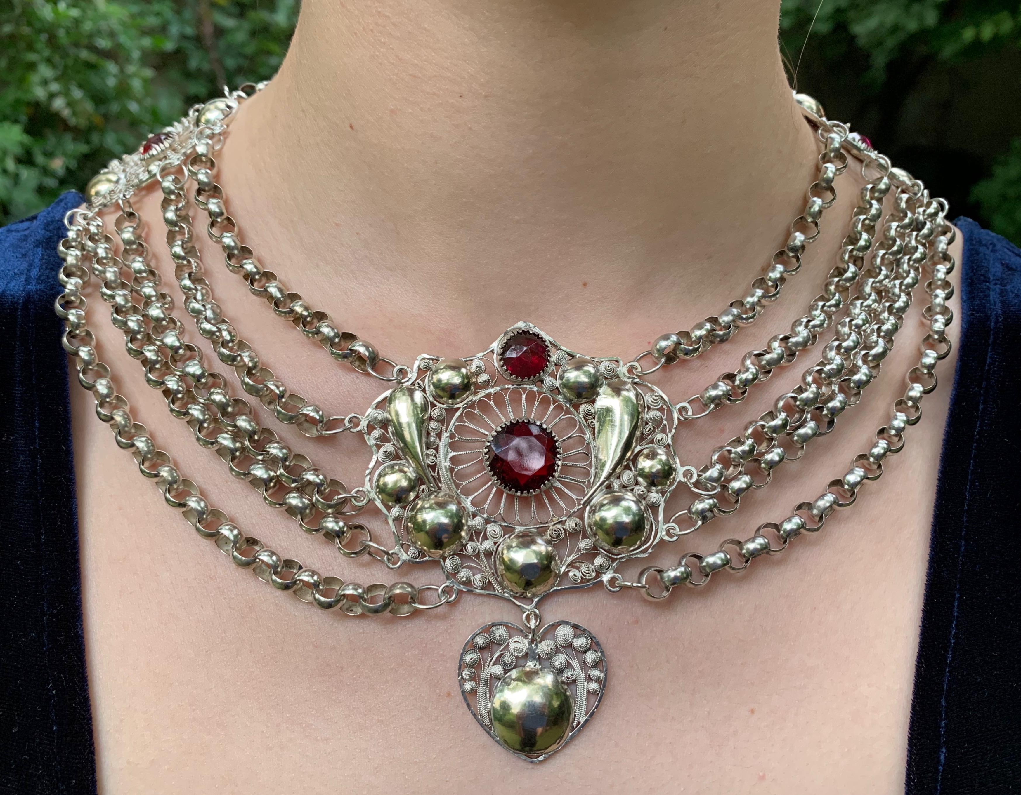 This outrageous silver necklace consists out of four rows of belcher chains and three ornamental plaques.  A center piece in the shape of a flower is decorated with embossed gilt ornaments and flowers made out of silver wire. They are grouped around