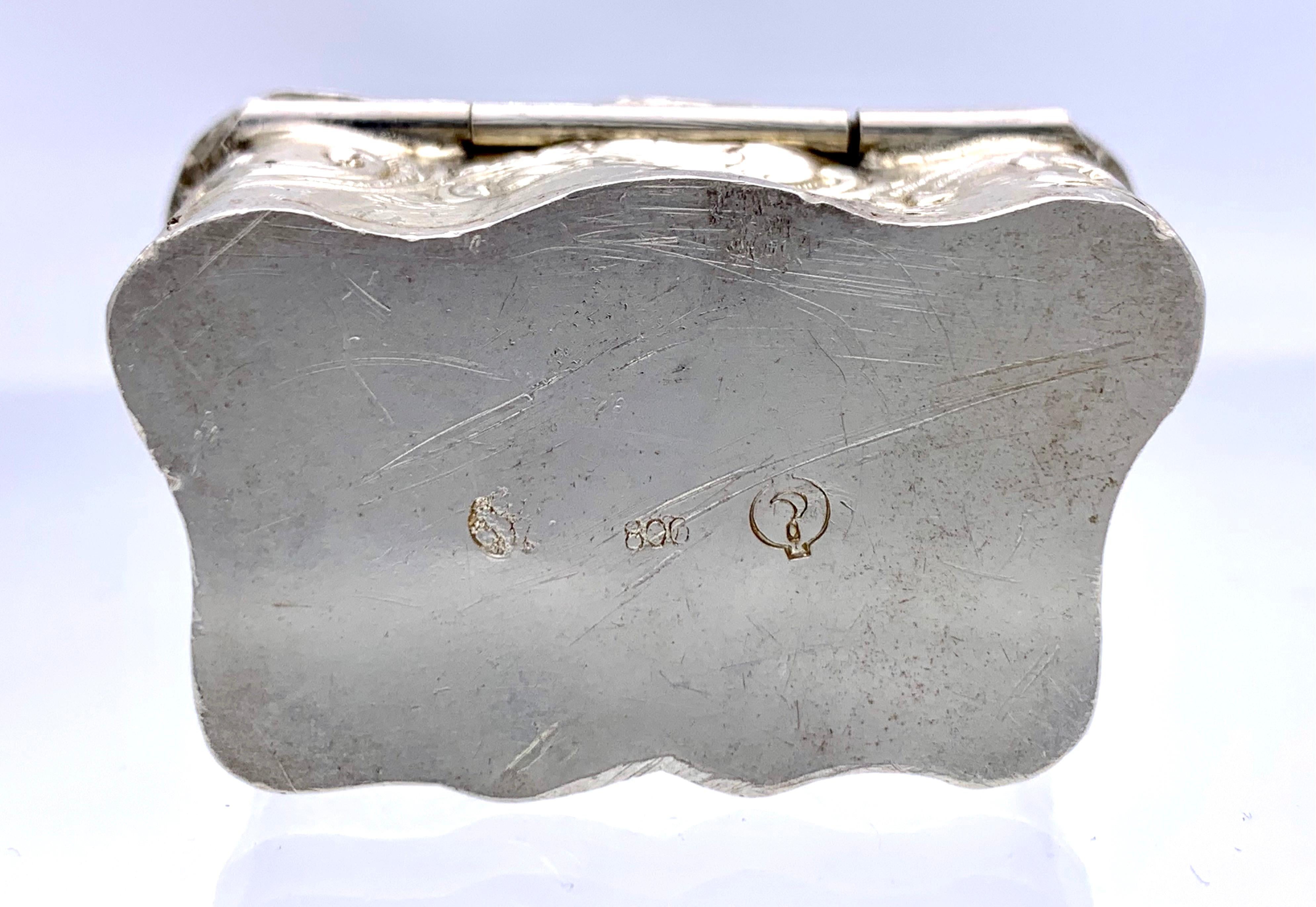 This small silver box is decorated with a romantic pastoral scene. A young woman wearing a straw hat, a bird sitting on her left shoulder is holding a basketwith her right arm. .  A young man is standing in the centre of the scene, leaning on a