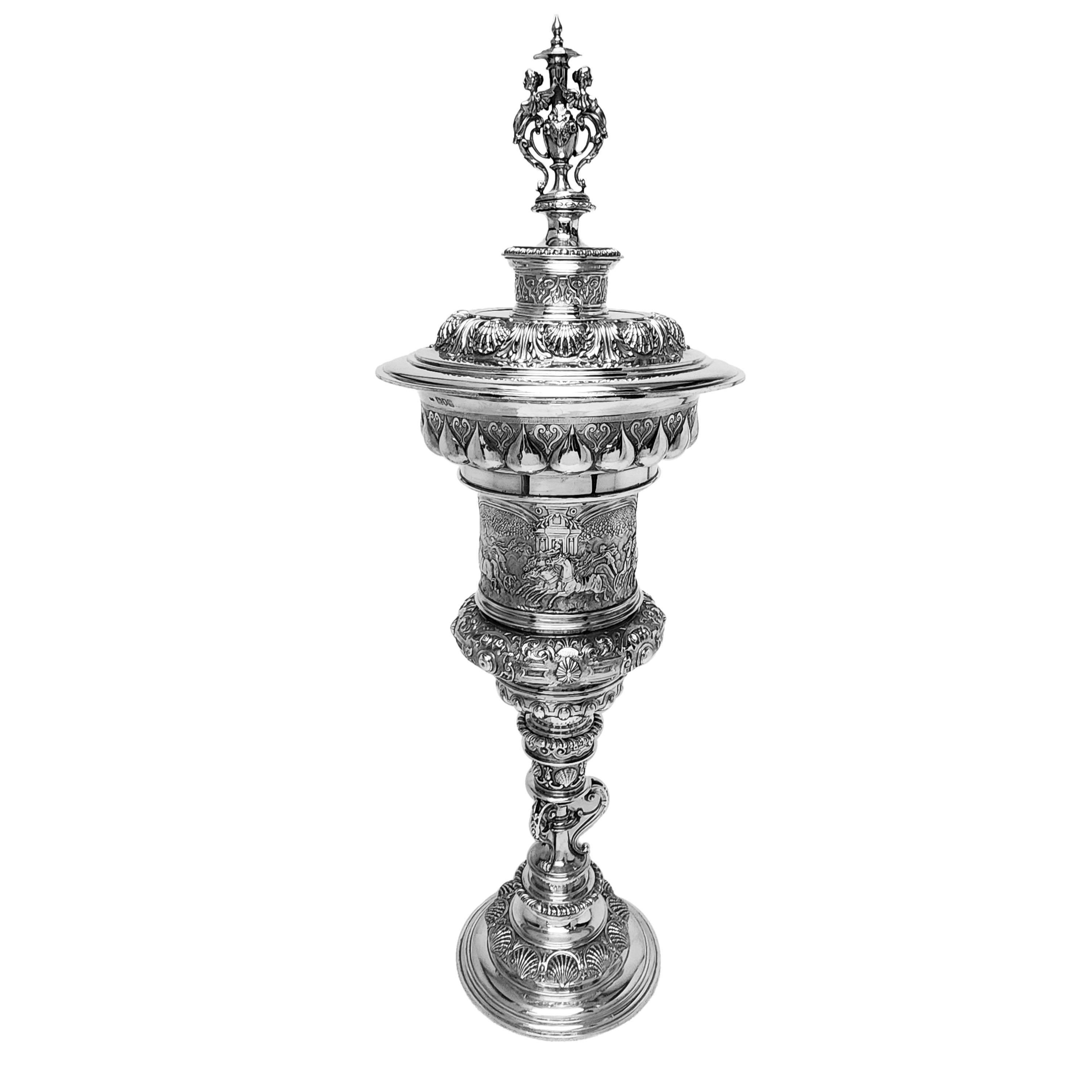 A magnificent Antique Sterling Silver Steeple Cup in the style of the original steeple cups of the early 1600s. The Cup is embellished with rich, detailed chased designs. The Cup has a central band is a frieze engraved with a classical chariot race.