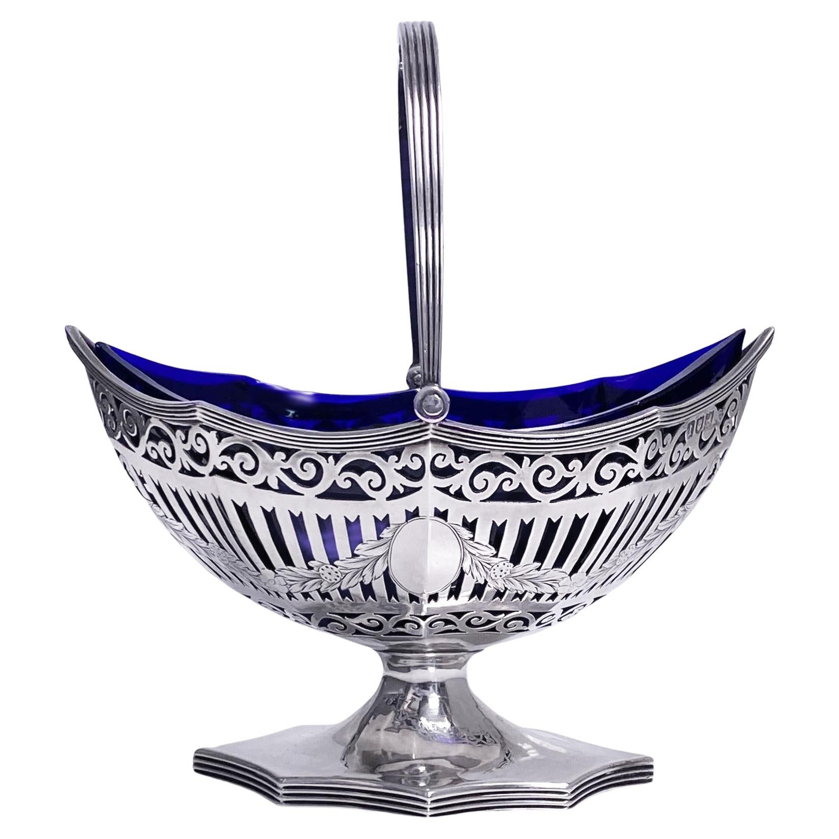 Antique Silver Sugar Basket with cobalt blue glass liner, London 1906 Haseler Bros (Edward John Haseler and Noble Haseler). The pierced swing handled basket of oval scalloped with eight panels surround design, liner conforming in shape. The base