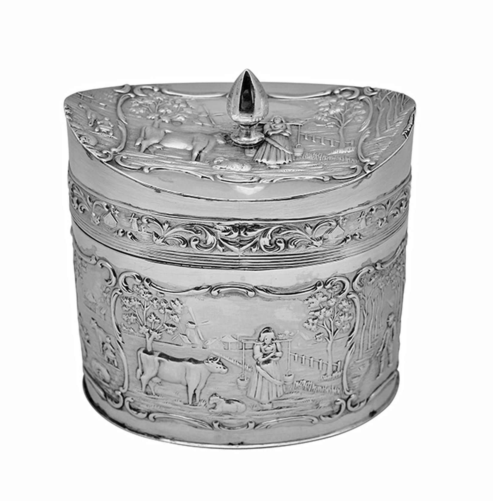 Antique silver tea caddy, H. Hooykaas-Schoonhoven Silber Fabrik, Netherlands circa 1900. Oval shape with hinged and concave cover. Chased and engraved scenes of country life in scrolled frames, milkmaids and cows against a background of windmills