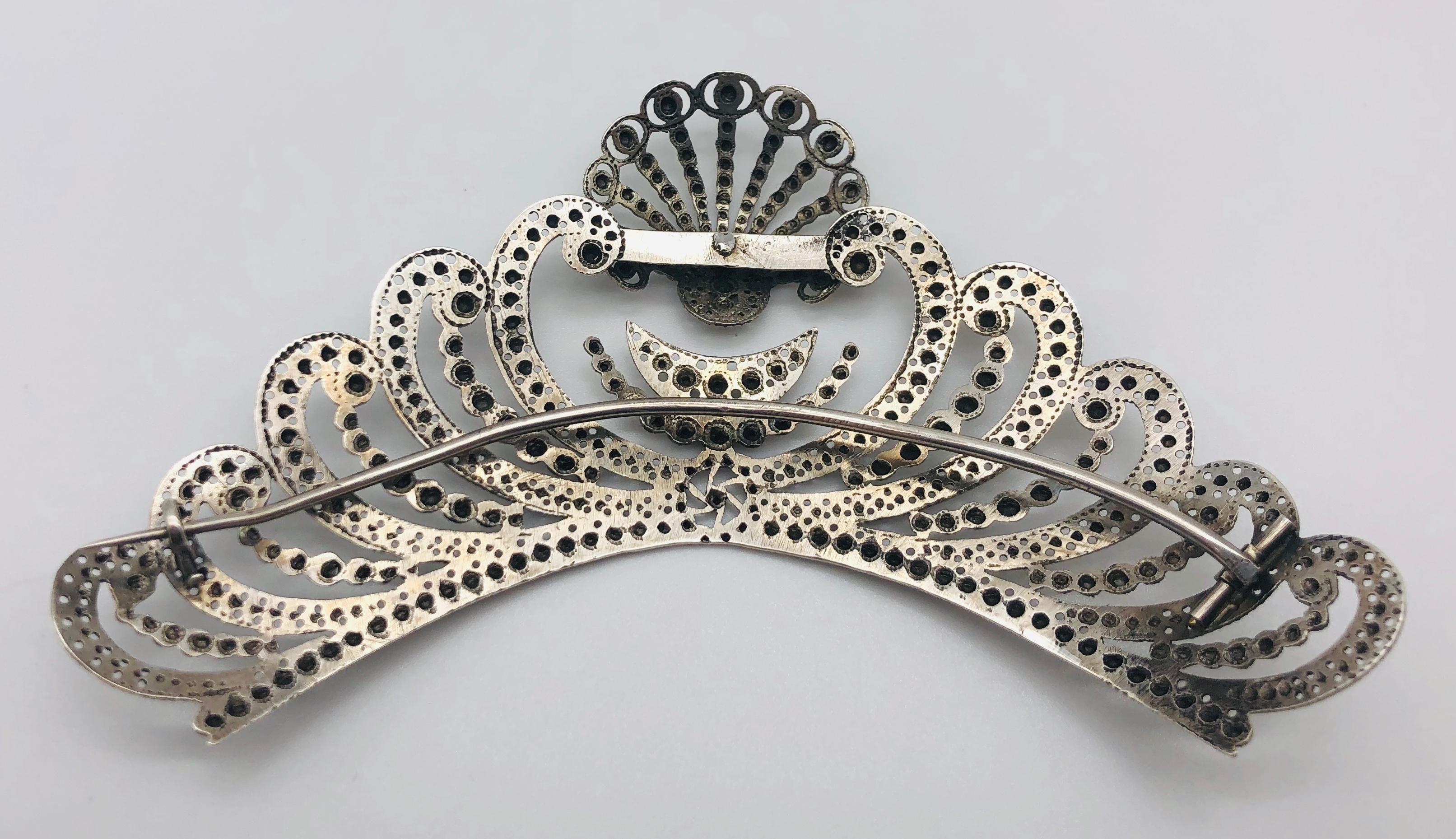 The head tiara ornament is made out of silver and decorated with a scallop, a crescent and a half moon. On top of a big stylised heart sits a scallop. Left and right of the heart are eight wave like ornaments. The silver is embossed in a manner to