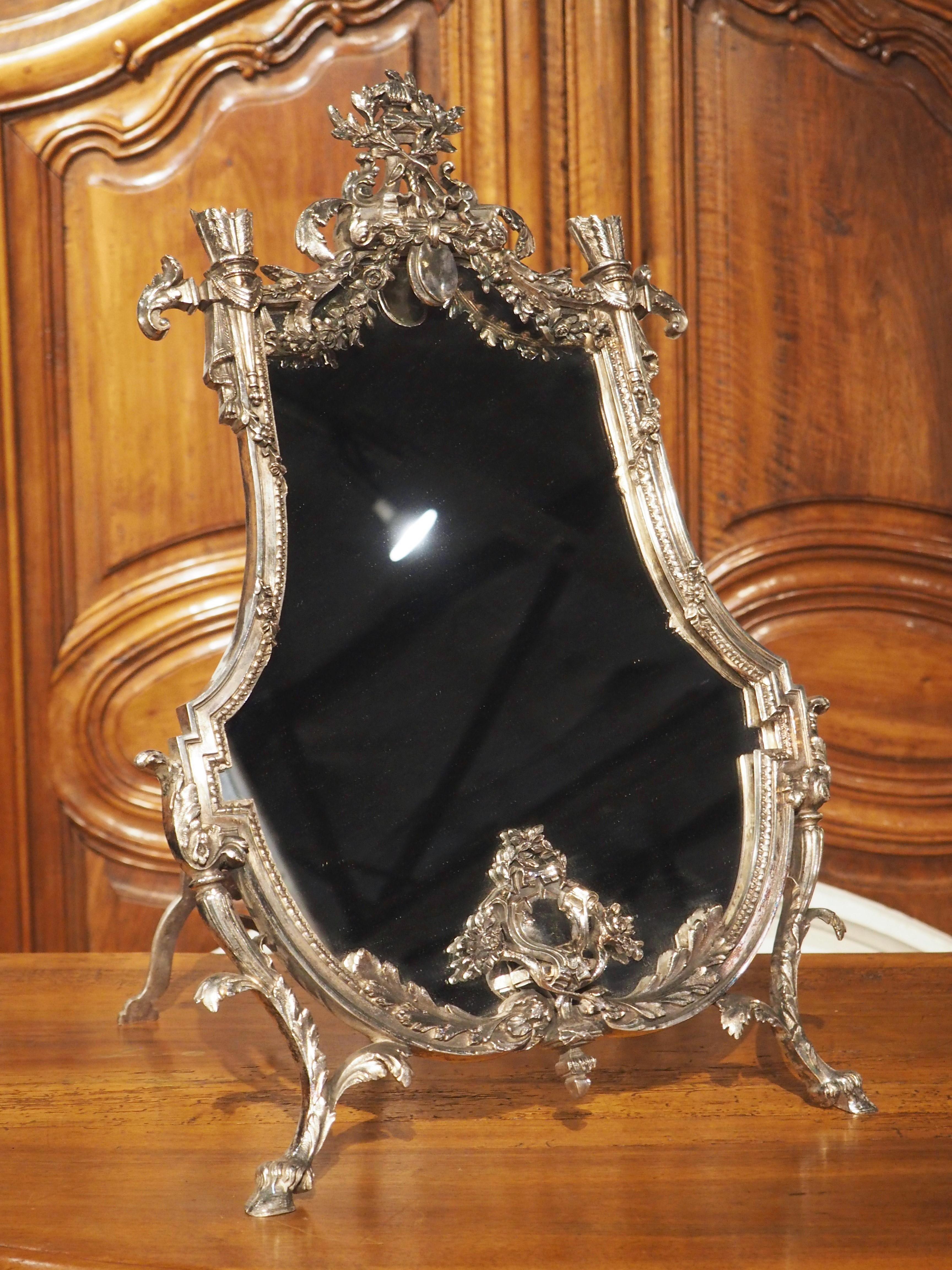 A unique production from the Napoleon III period, this silvered bronze table mirror features Neoclassical motifs that were prevalent during the “Second Empire”. The mirror rests upon a symmetrical two-legged easel stand with pierced elements. Two