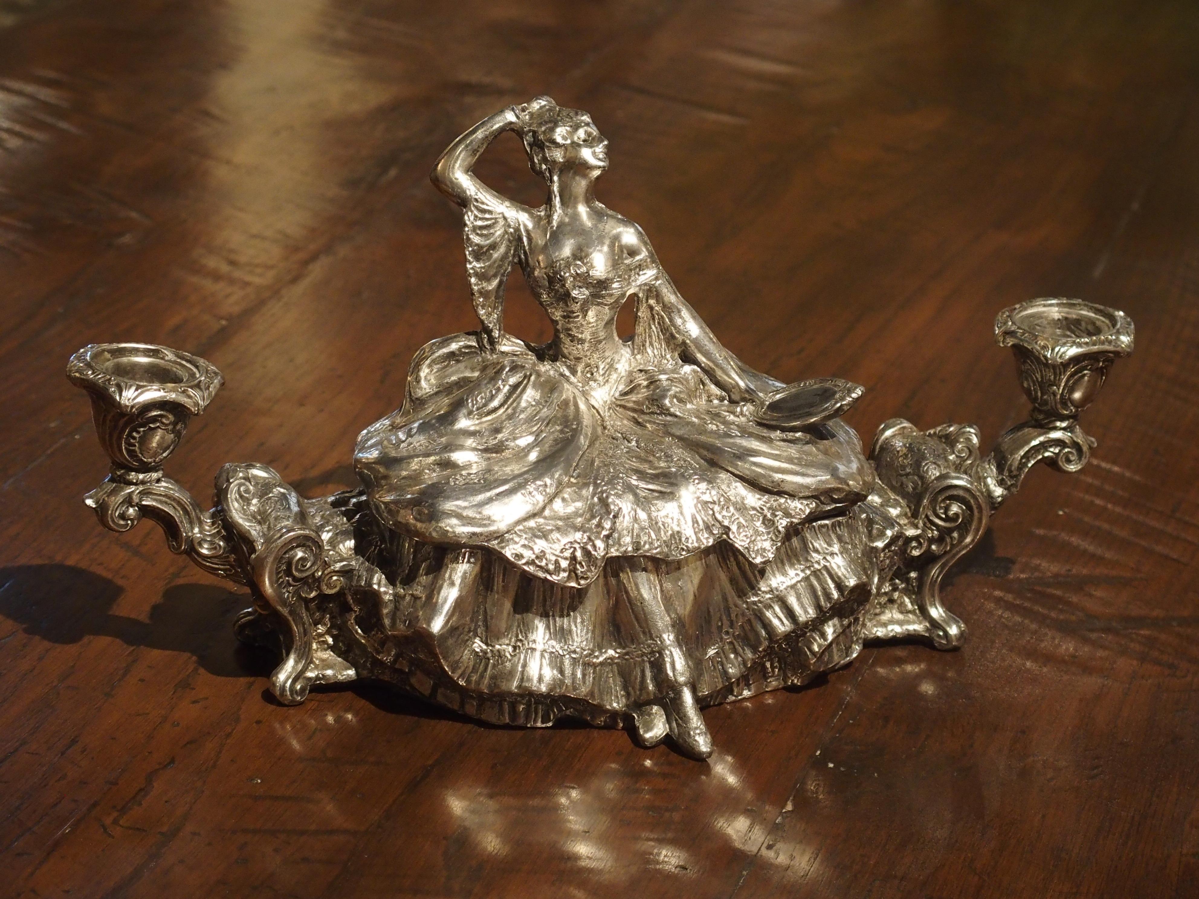 This is an early 1900s decorative silvered table or jewelry box. The top (once hinged), is removable, and there are C-scroll candleholders at each end. The subject is a woman seated on a banquette looking into a hand mirror. She wears a large