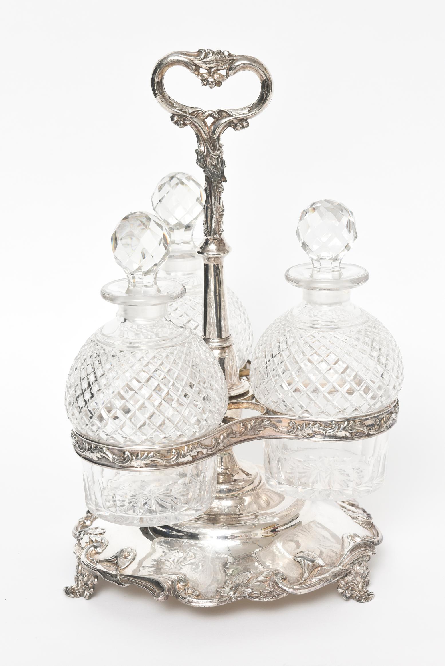 Ornate floral silver plate tantalus set featuring 3 cut glass bottles with a stand that comes apart into 3 pieces for easy storage. The stand has 3 feet so that it stands proudly on a table. The bottles measure approximately
7.5” x 4”.