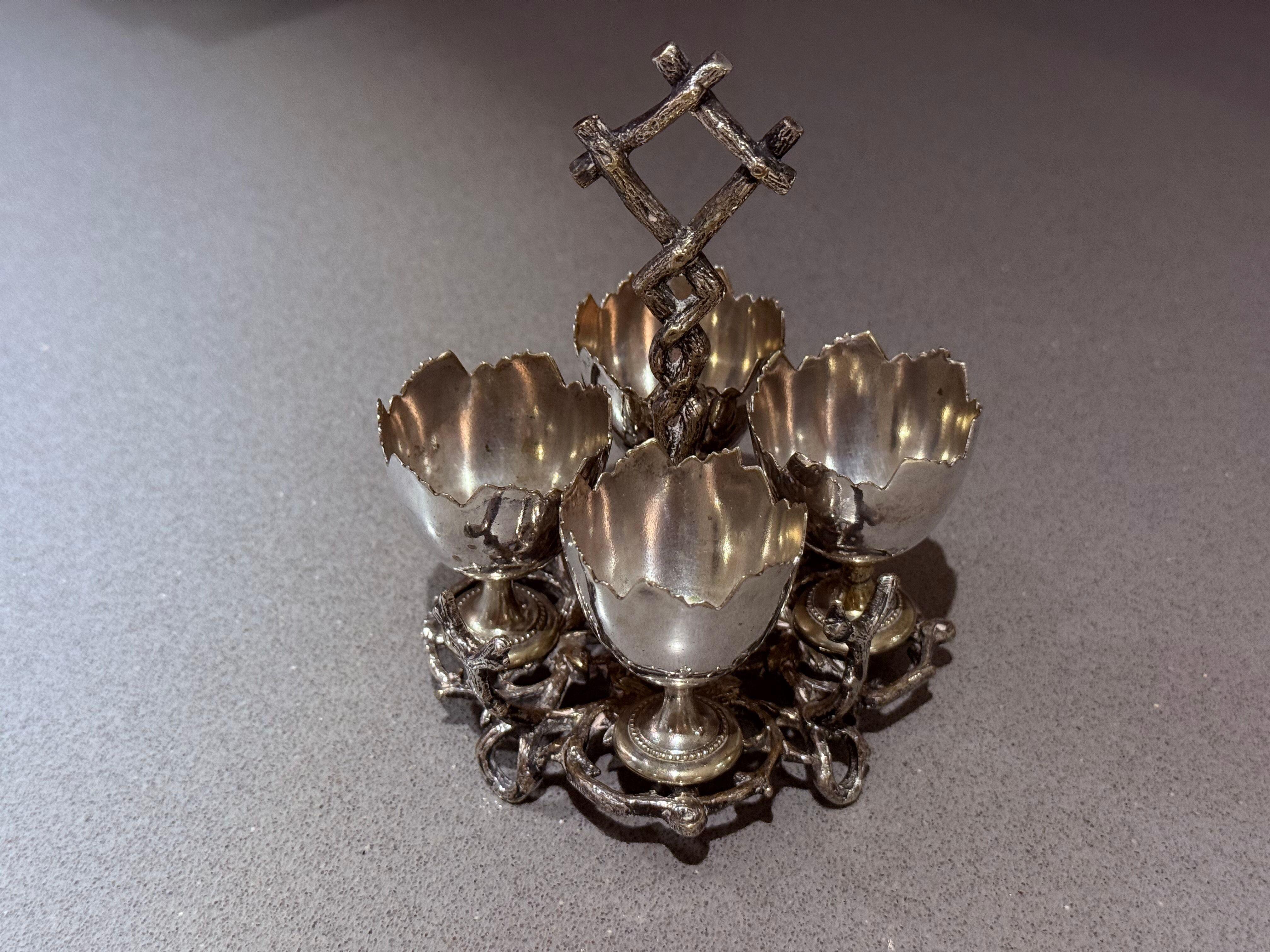 Antique Silver-Plated Egg Cup Stand with Four Holders, Ornate Victorian Style
A striking antique silver-plated egg cup stand featuring four beautifully scalloped holders arranged around an ornate central stem with an intricately designed lattice