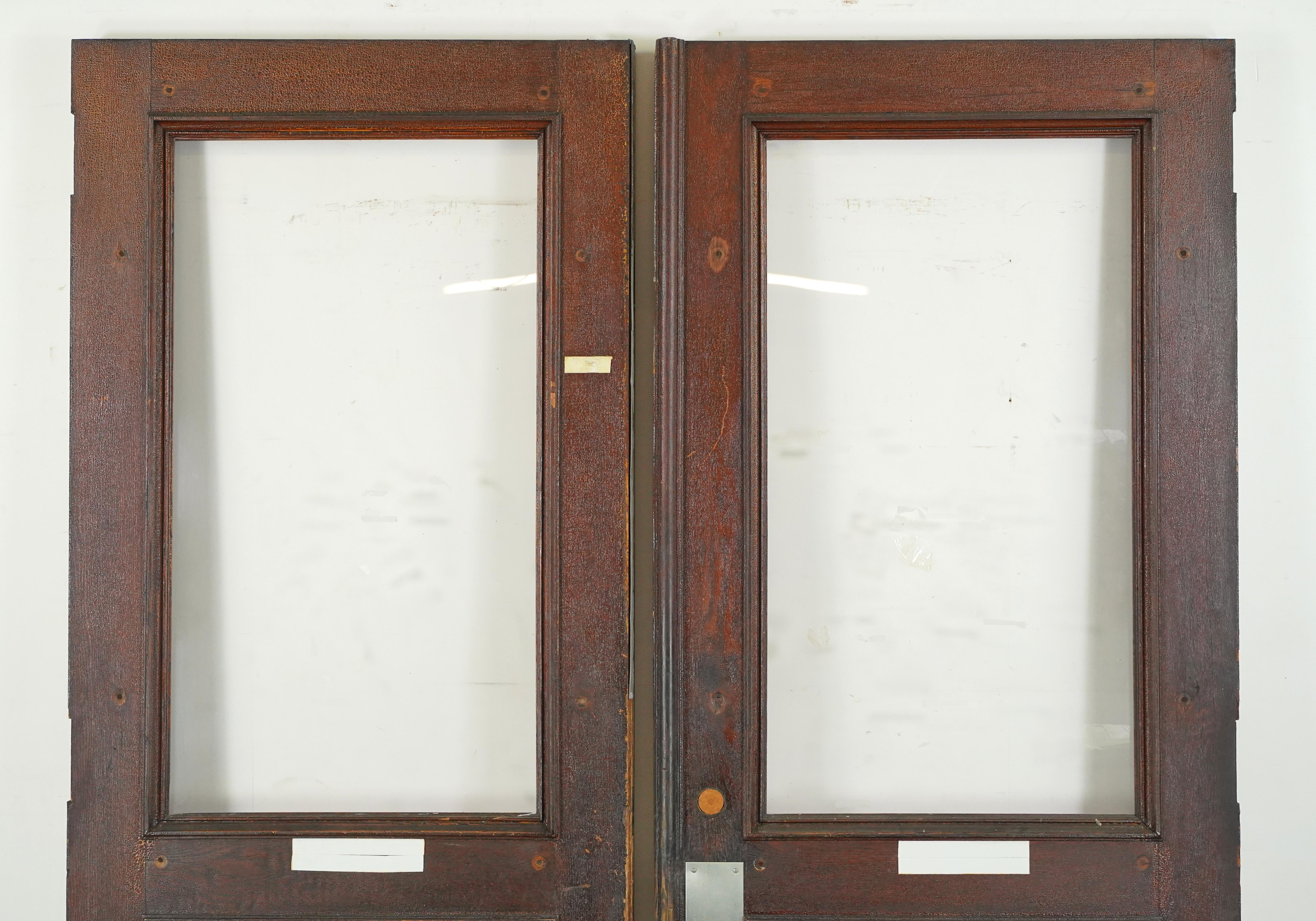 1850's entry double doors with a dark and medium stain on each side and half glass panes. The doors are in good solid condition with surface wear. Please refer to the pictures for a full view of the condition. Priced as a double. Some original brass