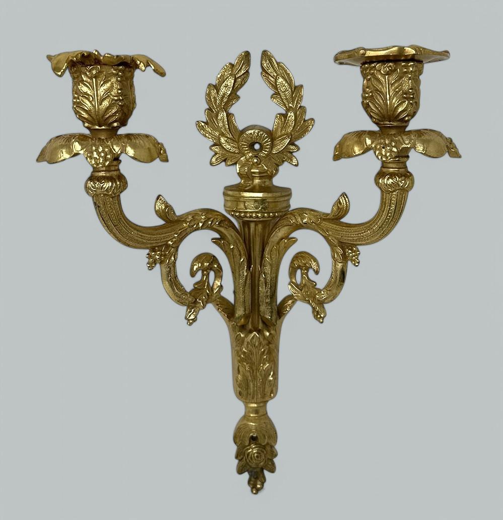 Lampada a candela da parete a due bracci in bronzo dorato di alta qualità, di proporzioni compatte, di media grandezza e con un'altezza di circa 1,5 metri.  alla fine del XIX secolo. 

I due bracci a voluta con cappuccio a forma di foglia partono da