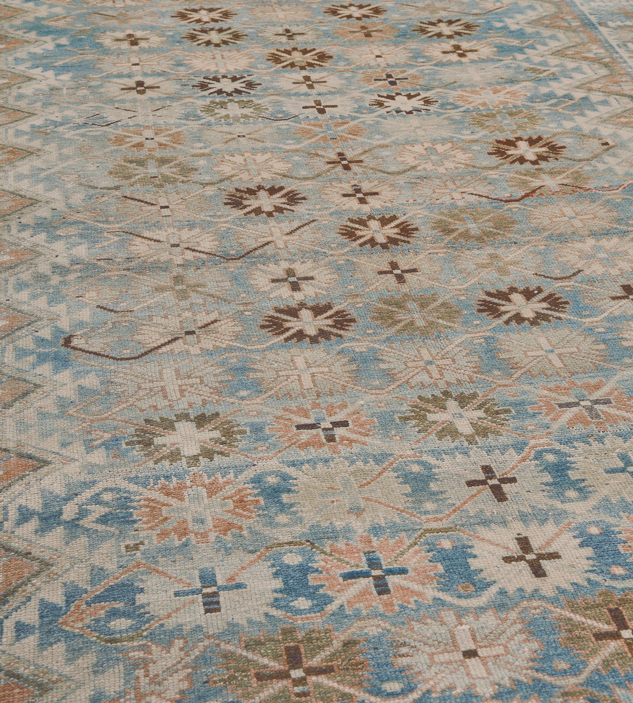 This antique Malayer rug has a shaded sky-blue field with diagonal rows of terracotta-pink, chocolate-brown, ivory and mole-brown bold stellar flowerheads linked by a bold ivory angular interlocking vine, the terracotta-pink linked zig-zag spandrels