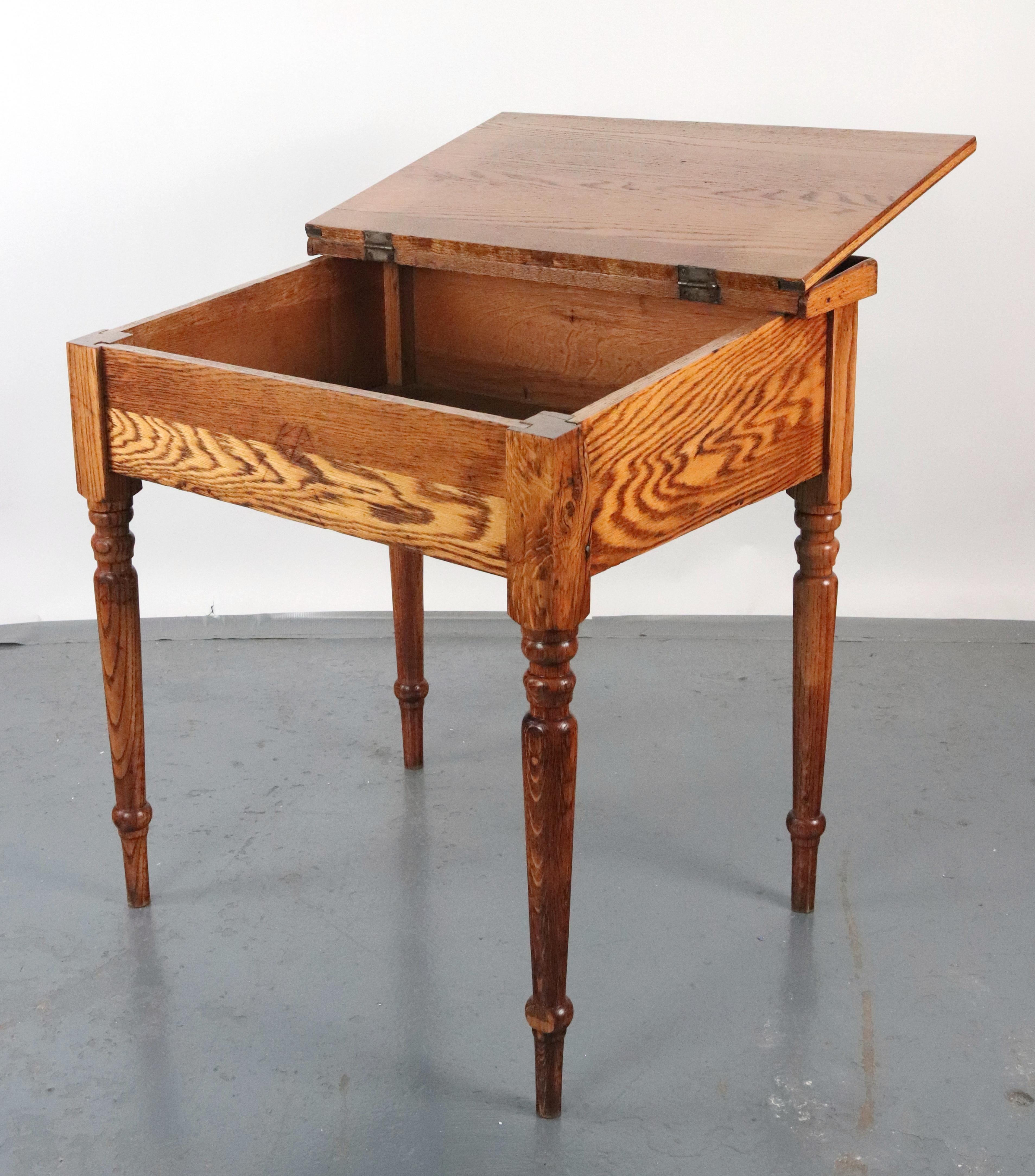 Bureau ancien en châtaignier dans un ton de bois moyen. Il est doté d'un plateau incliné à charnière qui révèle un compartiment de rangement et de quatre pieds tournés. Ces bureaux étaient utilisés dans les écoles ou par les employés de bureau. Bon