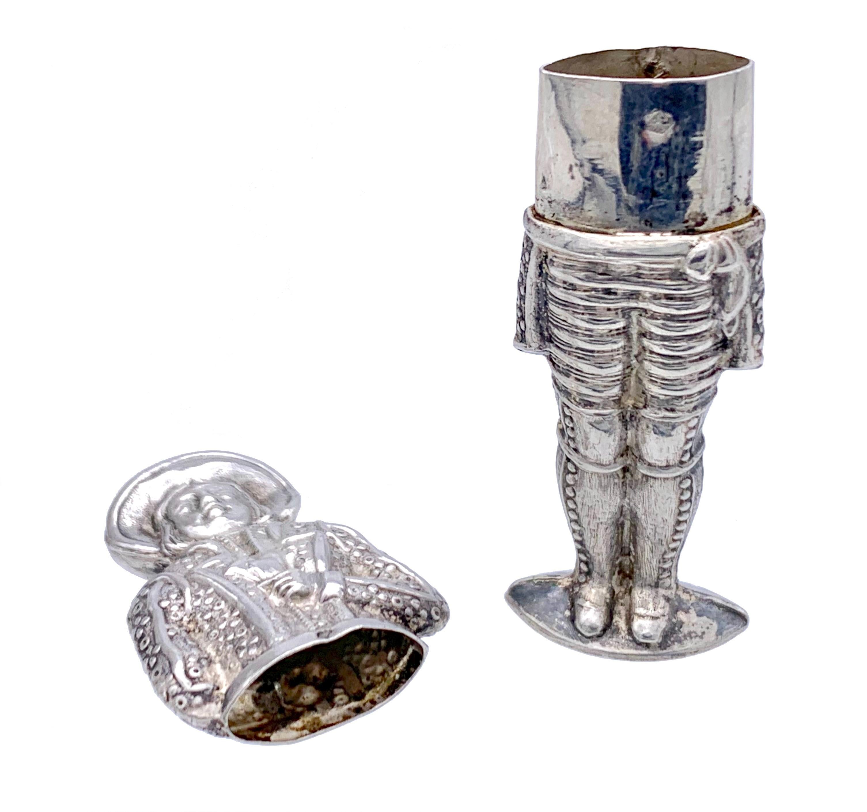 Charming silver Biedermeier needle case in the shape of a man wearing a hat, frockcoat  and gaiters. He is hiding his right hand, holding a playing card showing a diamond ace, behind his back.  