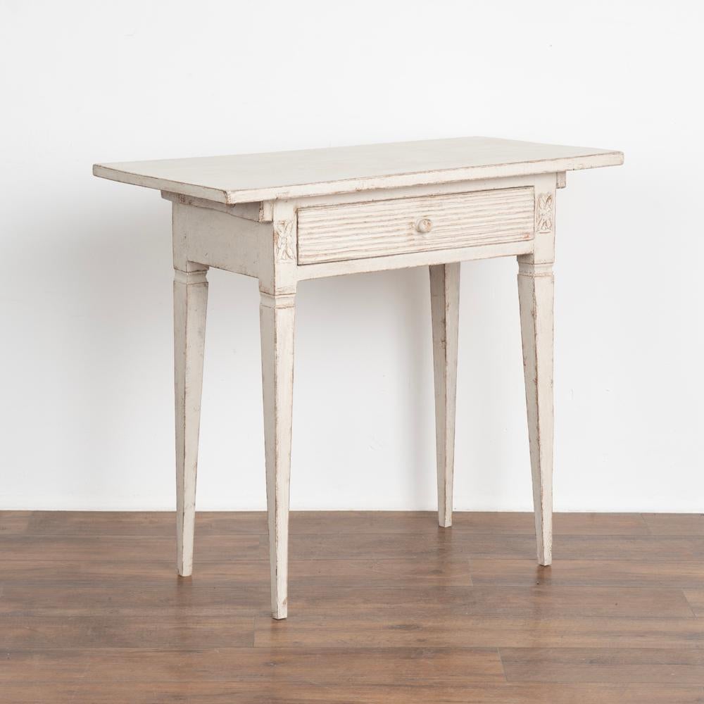 Antique Swedish Gustavian white painted small side table with drawer

Tapered legs and horizontal fluted carving along single drawer. May also serve as nightstand.
Restored, later professionally applied white painted layered finish lightly