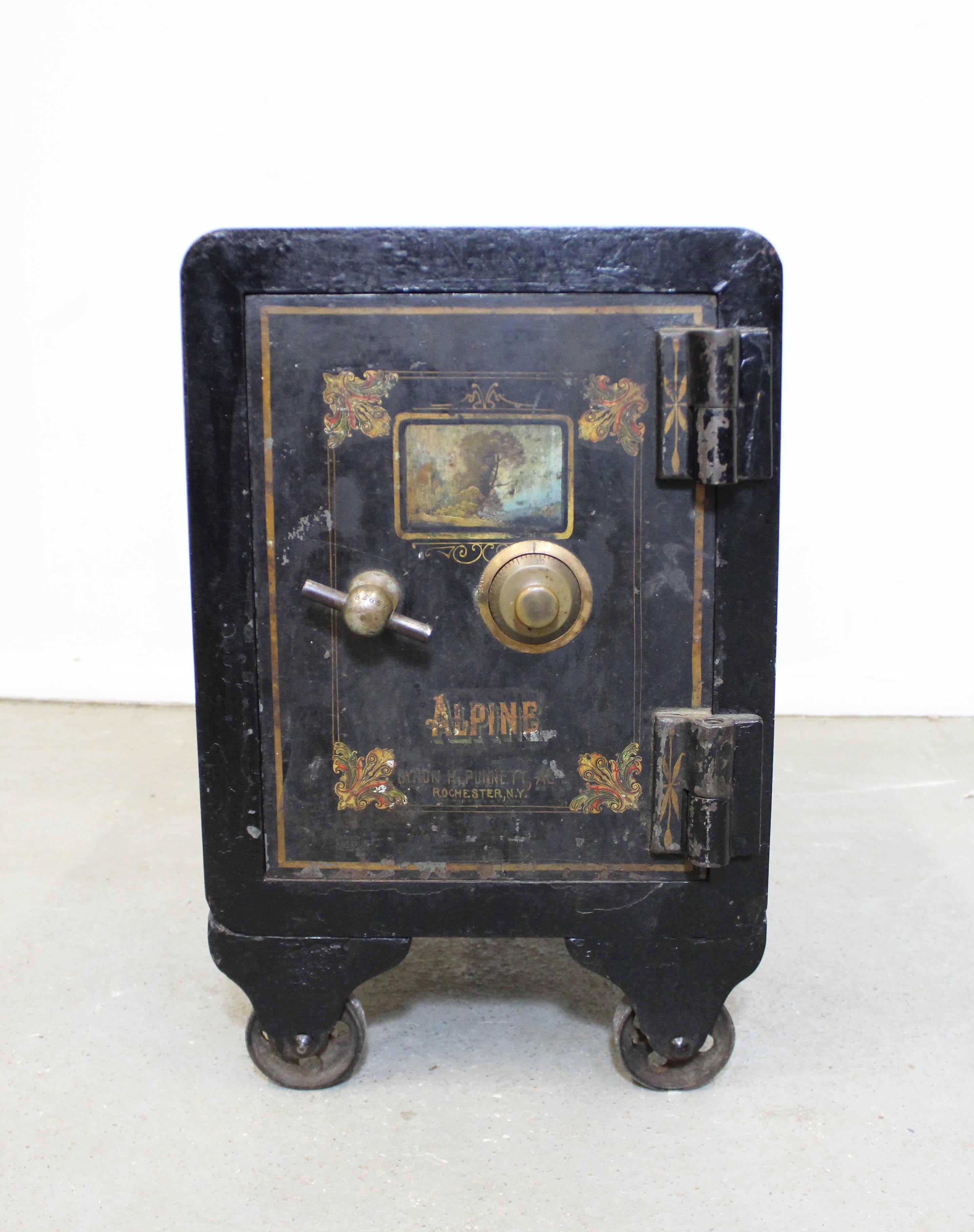 Offered is a small antique safe on wheels by Alpine. Made of cast iron, featuring original hand painted door. Inside features small compartments including one drawer and door with key. Combination is on the back. Functional and usable. Shows age