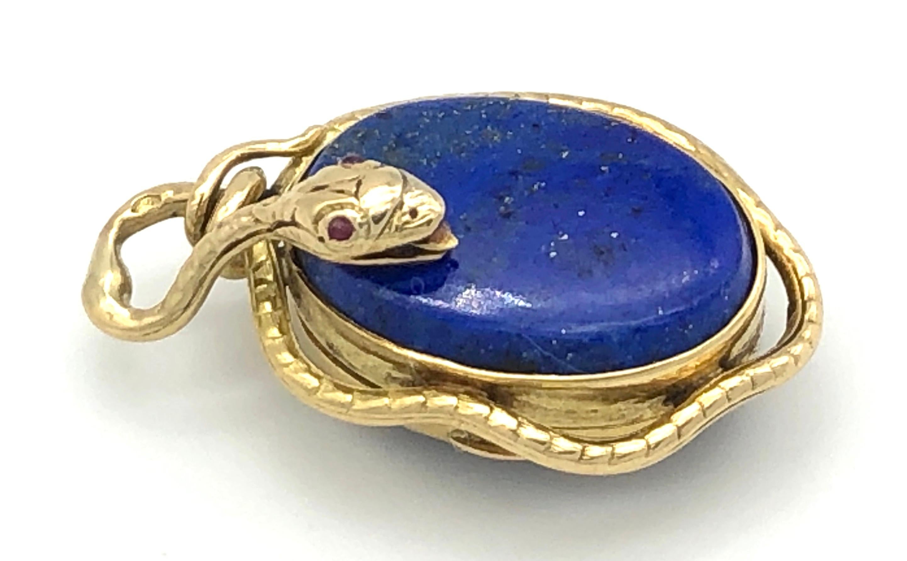  A golden snake with two rubies as eyes is curling itself around a  locket made out of 18kt gold. Either side of the pendant is decorated  with an oval lapis lazuli cabochon. The pendant is the work of a french goldsmith.

