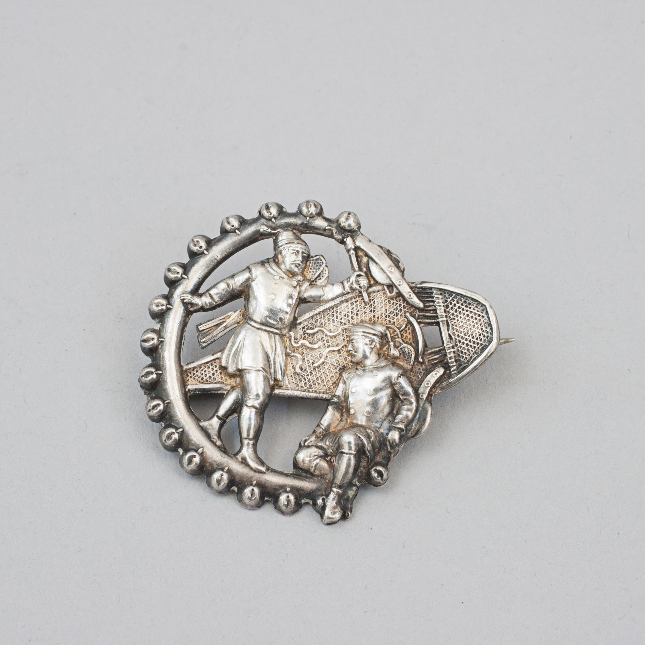 Snowshoe Brooch Or Pin.
A very nice piece of antique winter themed jewellery, a broach in the form of a snowshoe with two gentlemen. The surround is in the form of a leather strand with sleigh bells attached to it. The rear has a clasp and is
