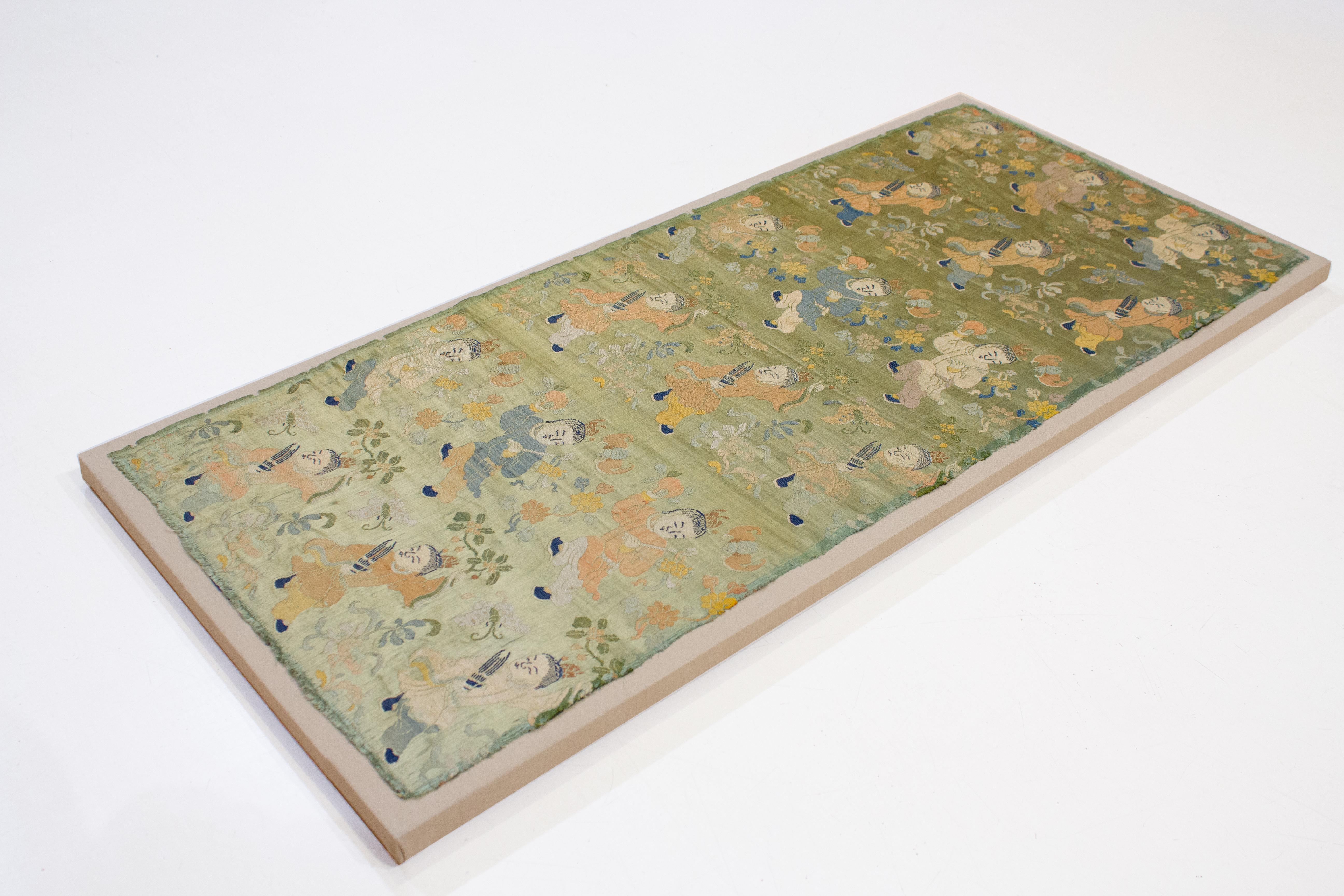 Woven in the age of the third Qing Emperor Yongzheng (1722-35), this delicately coloured precious silk brocade is embellished  by three parallel and offset rows of children holding a cornucopia of auspicious symbols. In the first horizontal row, the