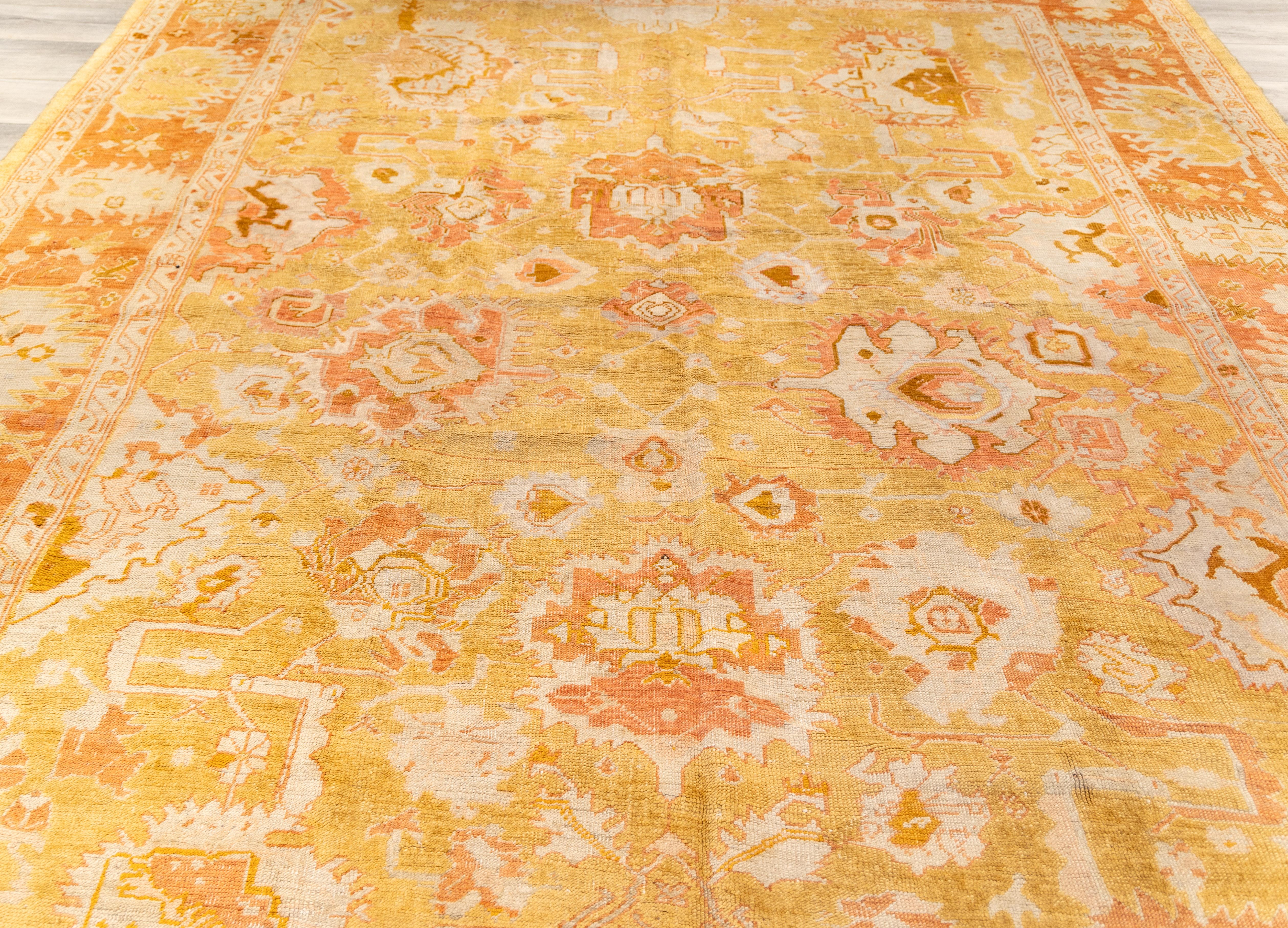 antique Oushak rug early to 20th century with warm color palette dominated by soft golds, saffron yellows, and muted oranges. 

The central field is a golden yellow, with faded and distressed areas giving it a soft, aged patina. With a stylized