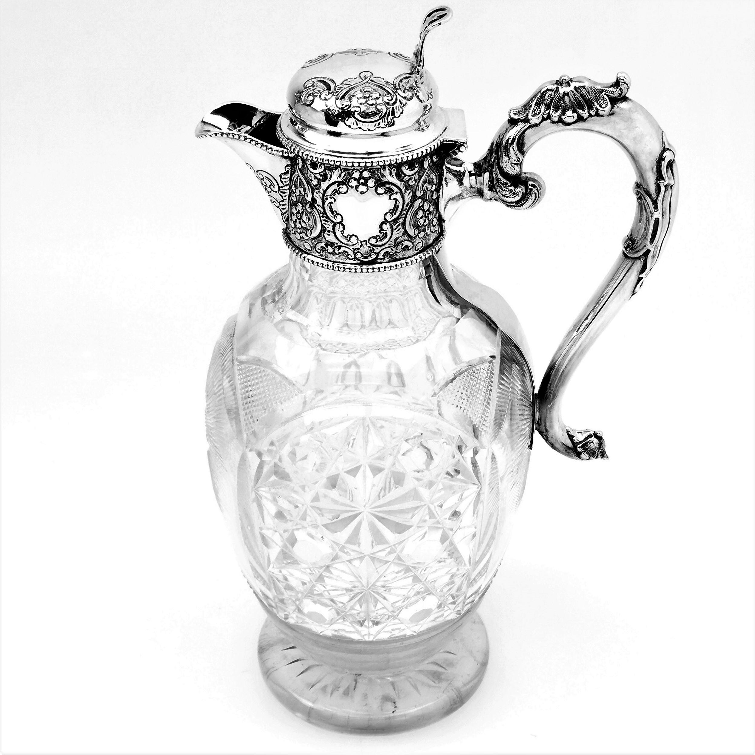 A lovely antique sterling silver and cut glass claret jug. The wine jug has an elegant cut glass body featuring a star burst pattern opposite the handle. The claret jug has a solid silver collar, handle and hinged lid. The claret Jug features a