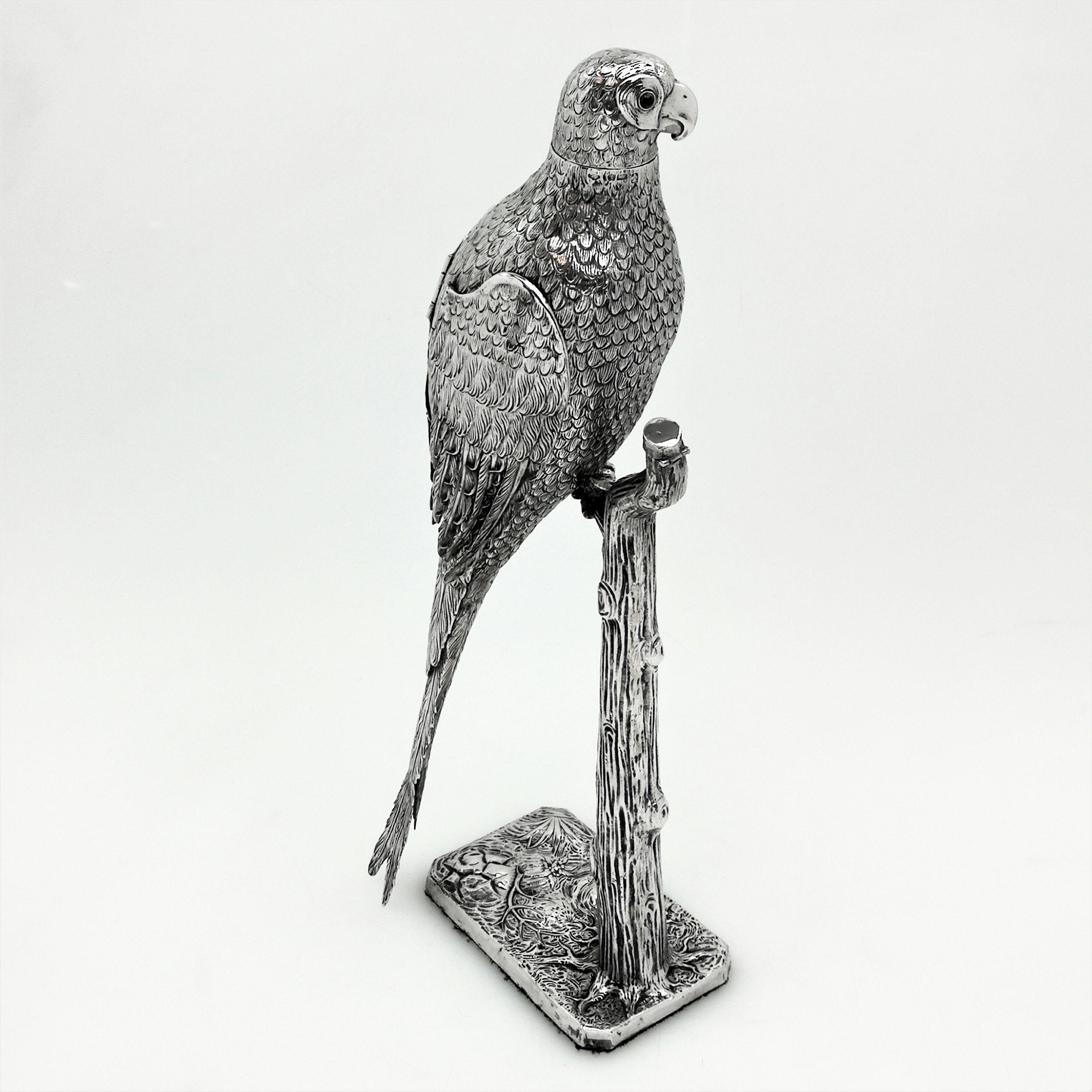 An impressive antique German solid silver figurine showing a parrot on stand created with an impressive attention to detail. The parrot perches on a branch above a chased rectangular base. The parrot has hinged wings and has yellow and black glass