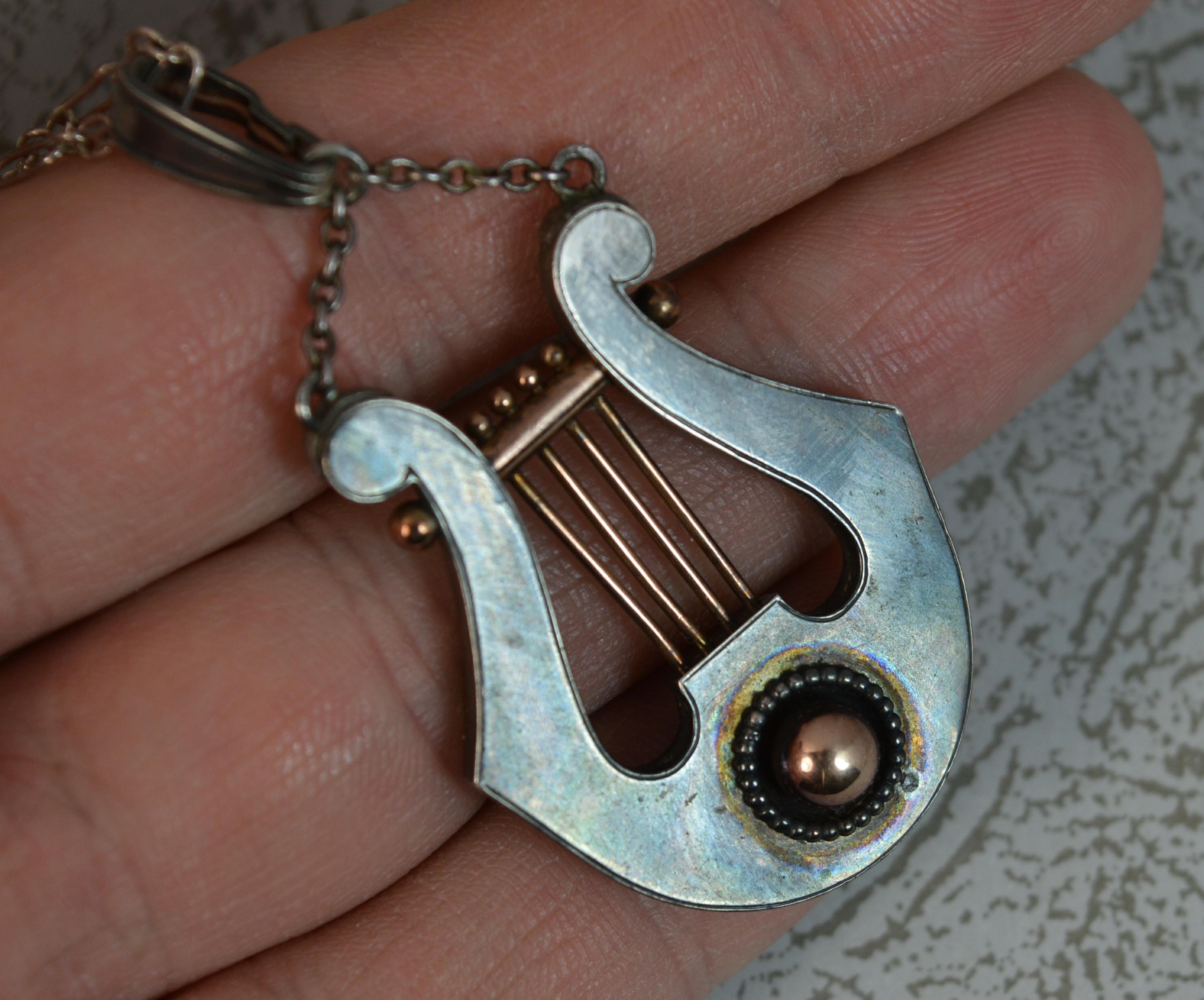 A Victorian period ladies solid silver pendant.
Designed with a lyre musical instrument. 
Modelled in solid silver with a wonderful gun metal like toned finish. With a rose gold ball to the centre of the centre piece and rose gold strings. 
Complete