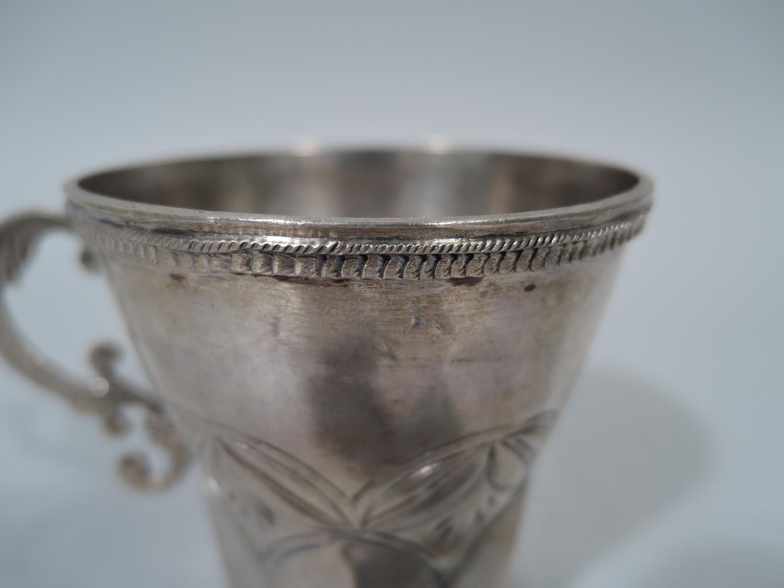 South American silver mug, 19th century. Curved top and faceted bottom with tooled arcade-inset lozenge border. Fancy leaf-capped S-scroll handle. Dentil rim borders. Unmarked. Weight: 3.8 troy ounces.