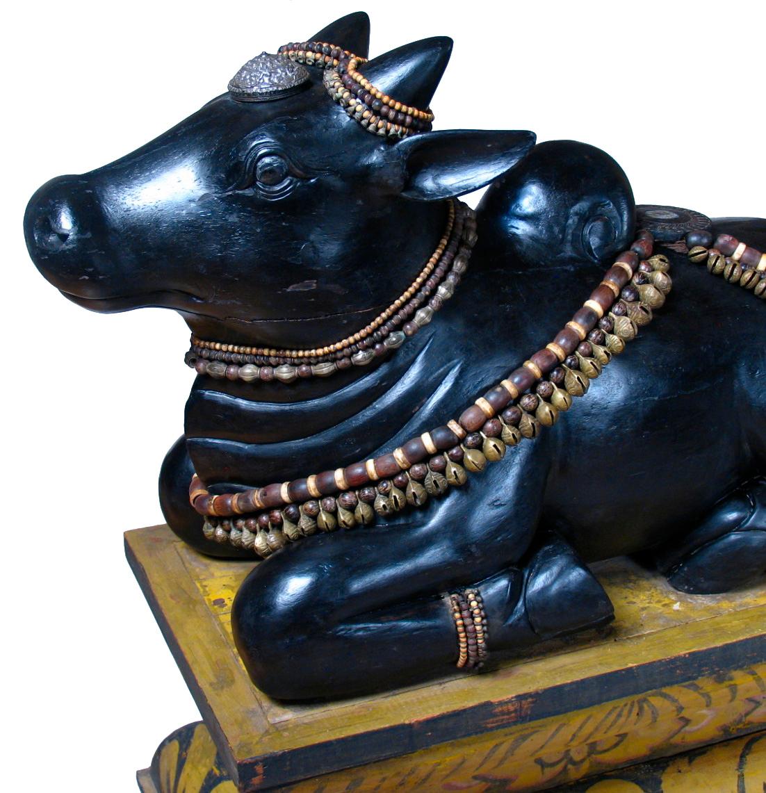 South Indian carved wood sculpture depicting the Hindu deity of Nandi, a recumbent black bull figure, known within the Hindu faith as the vehicle for Siva, often depicted in sculpture in a Hindu temple facing Lord Siva, often prayed to as a