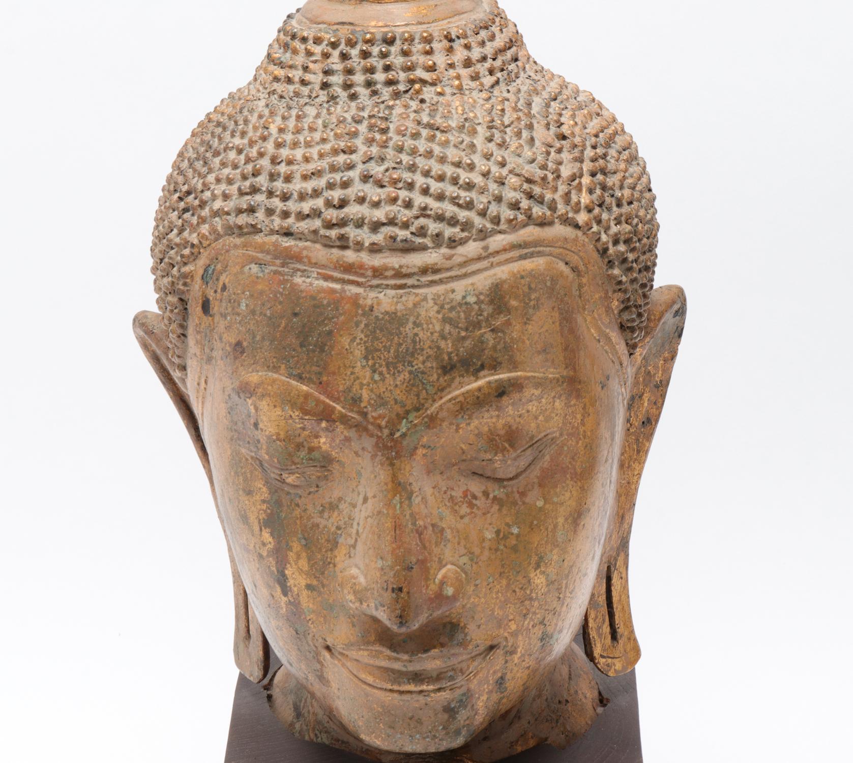 Thai or Cambodian gilt bronze Buddha head depicted with ushnisha and elongated earlobes, mounted on wood base.