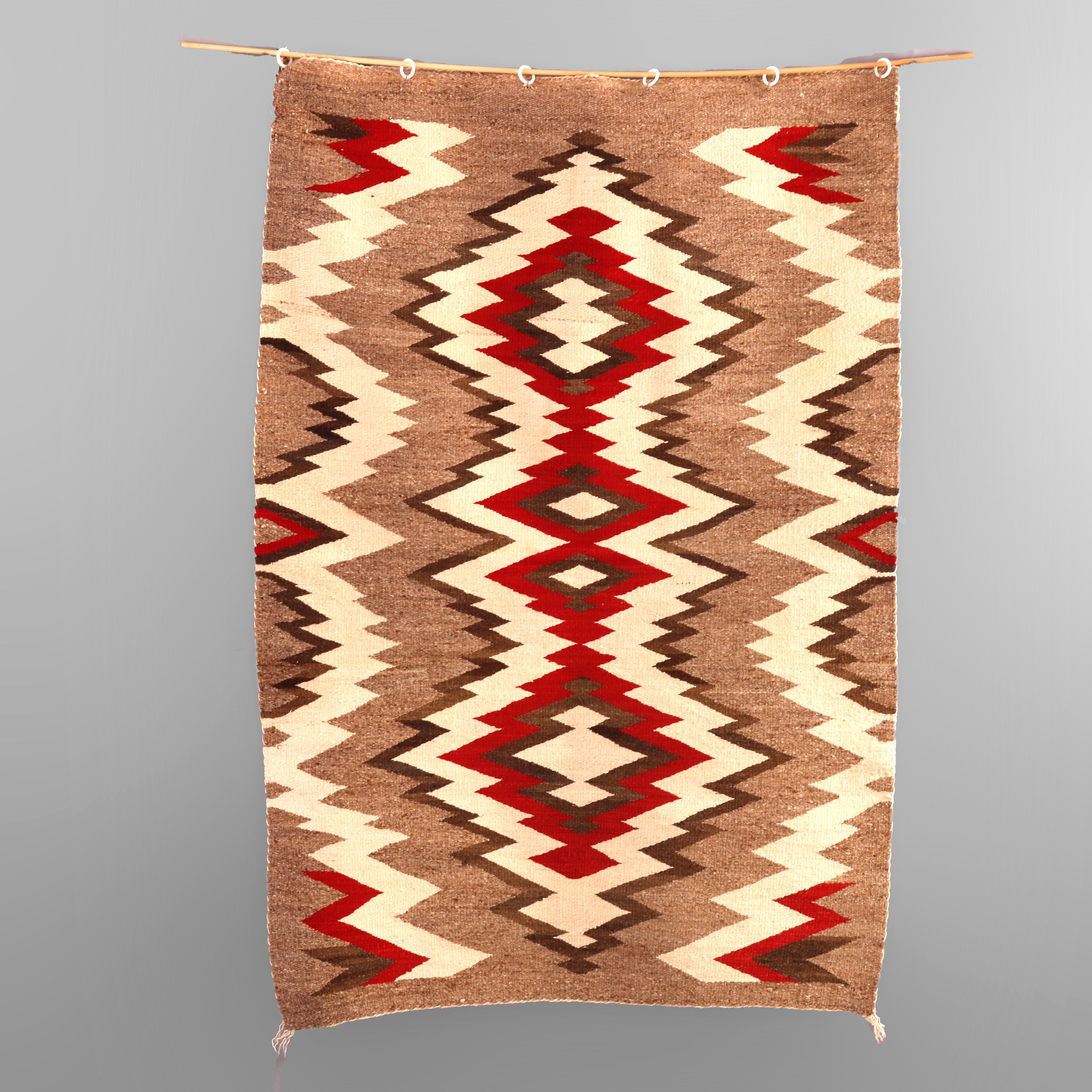An antique Southwestern Native American Indian rug offers wool construction with a geometric eye dazzler pattern in red, black and white on brown ground, c1920

Measures - 47.5'' L x 32'' W x .25'' D.