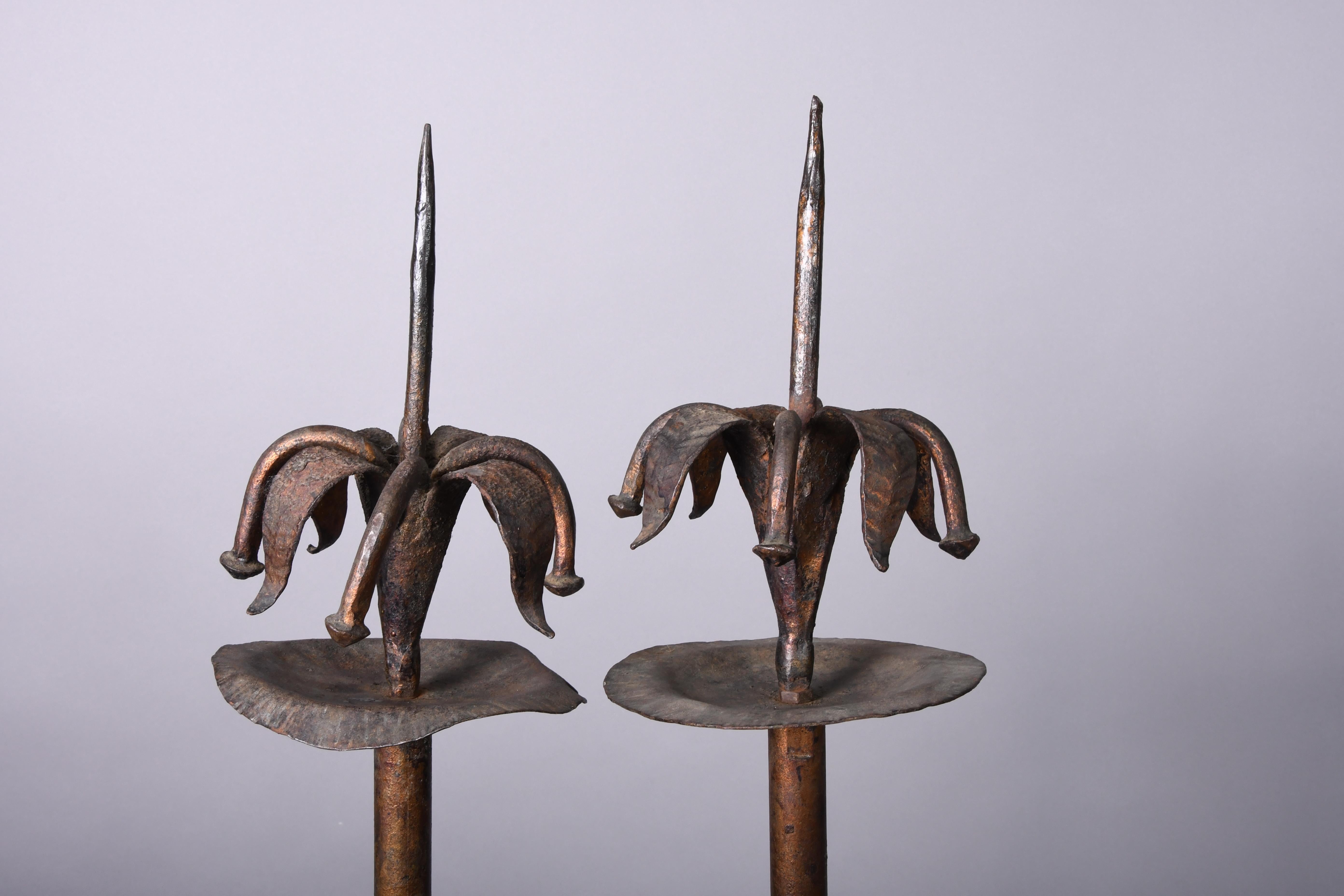 A pair of iron candleholders that around the pricket opens a flower. The stem ends on a tripod stand.