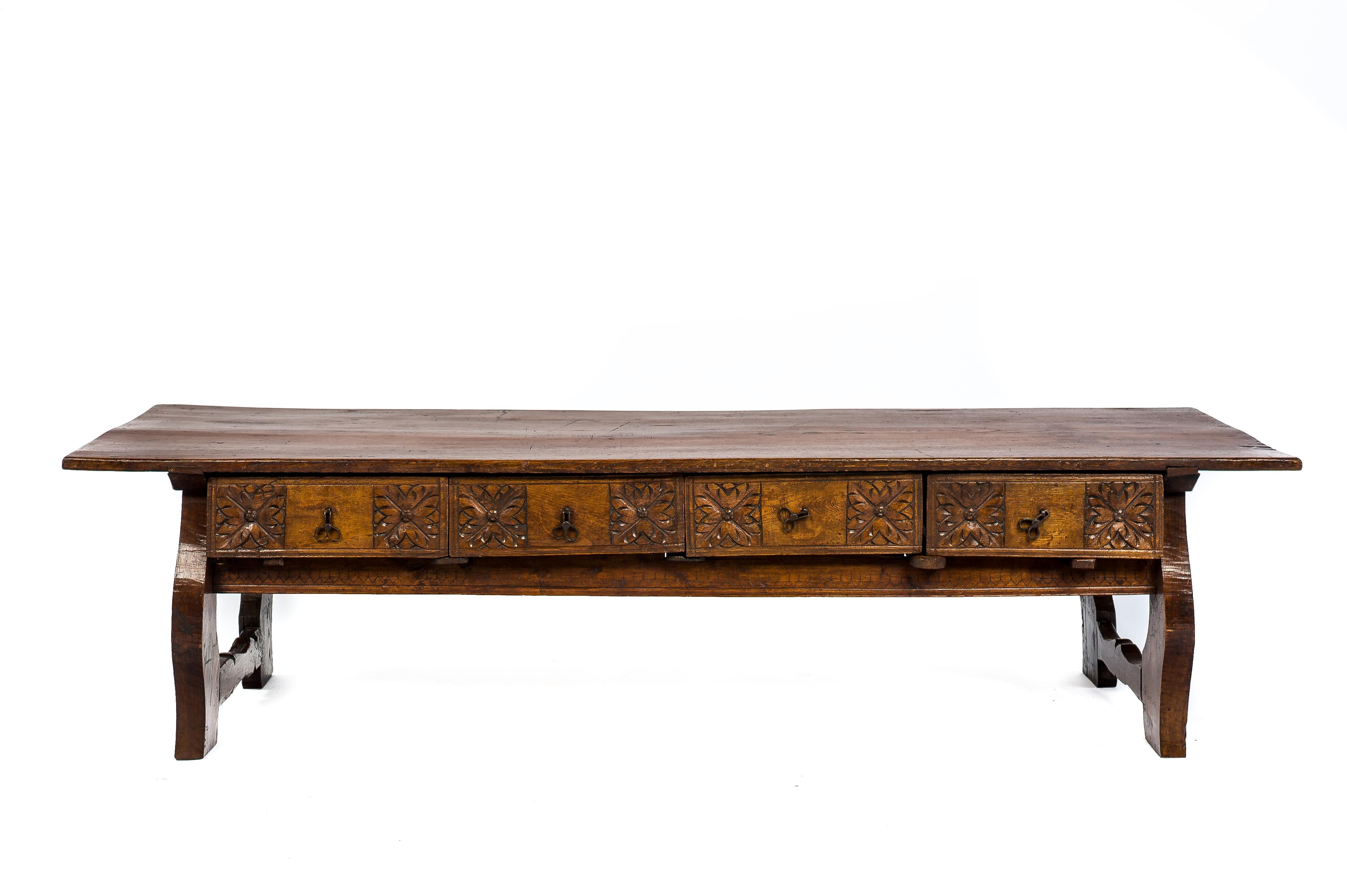 A beautiful Spanish Baroque style chestnut coffee table from the early 19th century. 
The table features four drawers with geometric hand carved flowers on the front panels. The hand forged drawer pulls are original to this piece. Underneath the