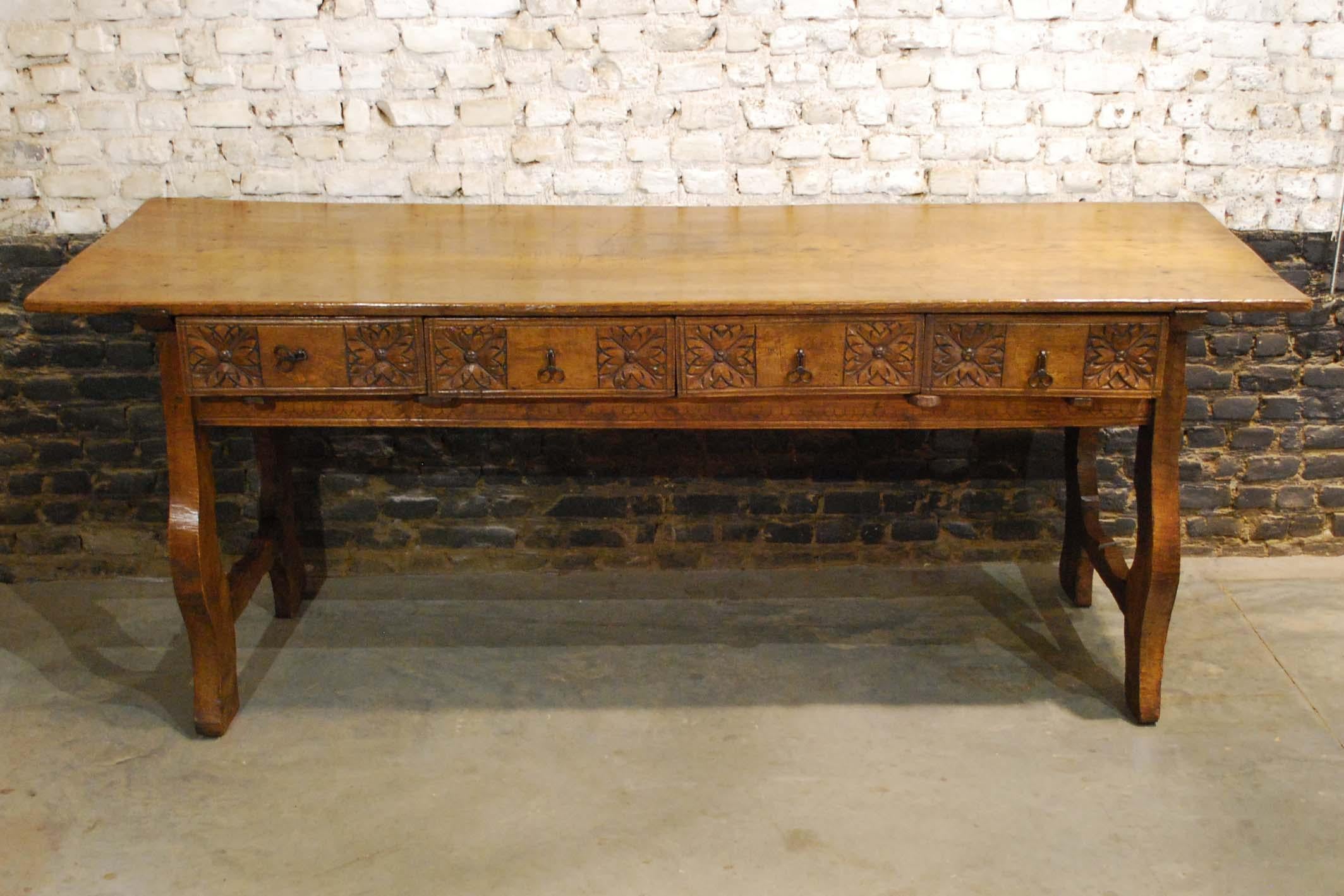 A beautiful and very authentic Spanish Baroque style chestnut table from the early 19th century. 
The table features four drawers with geometric hand carved flowers on the front panels. The hand forged drawer pulls are original to this writing