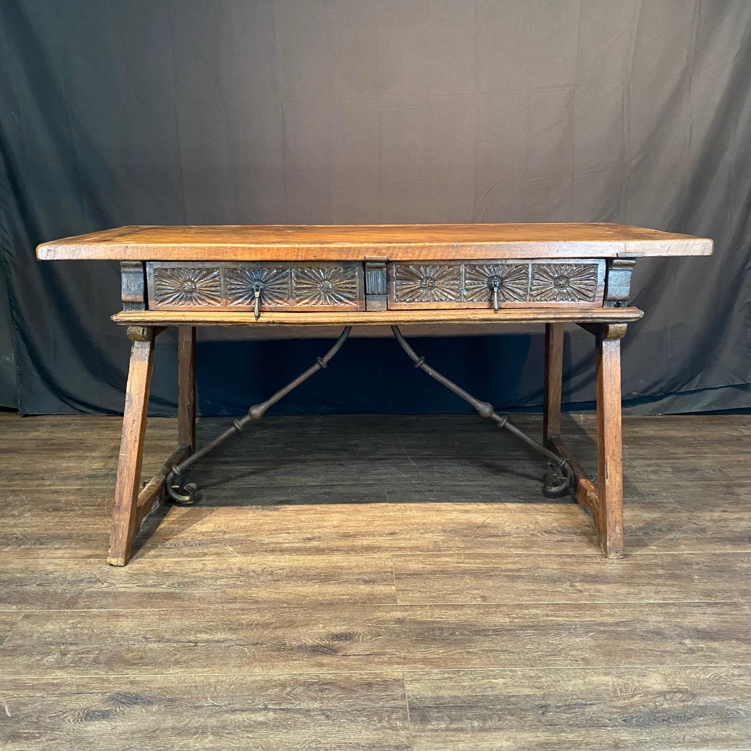 Magnifique bureau, table à écrire ou console baroque espagnole du début du XIXe siècle, en noyer massif, avec des pieds en lyre reliés par des brancards en fer forgé, et comprenant deux tiroirs avec une façade sculptée de tournesols géométriques et