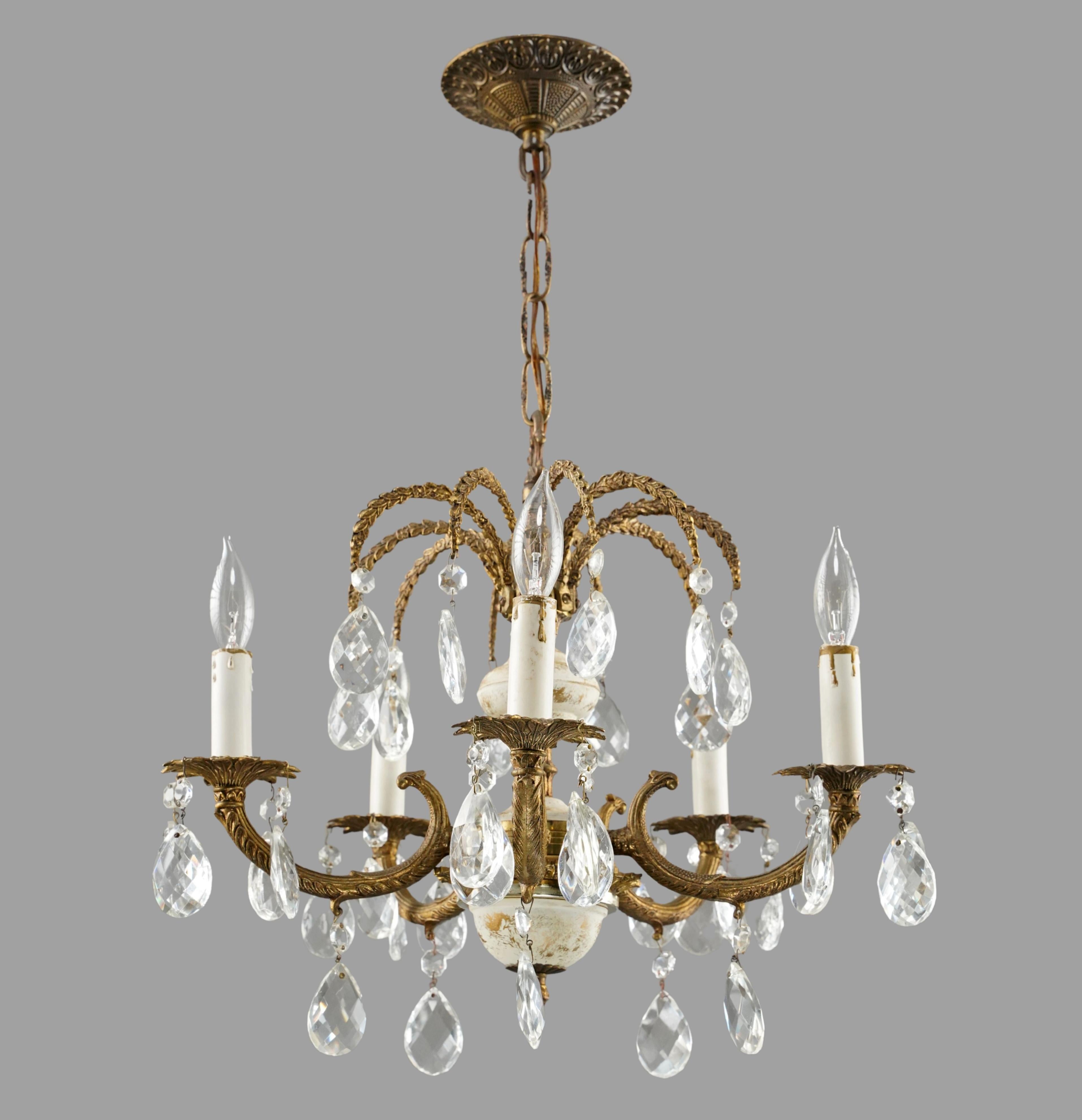 Araña de estilo español formada por un marco de latón ornamentado, elementos centrales de cristal blanco envejecido y cristales transparentes en forma de lágrima. Esta luz requiere cinco bombillas candelabro. La cadena es de acero. Limpiado y