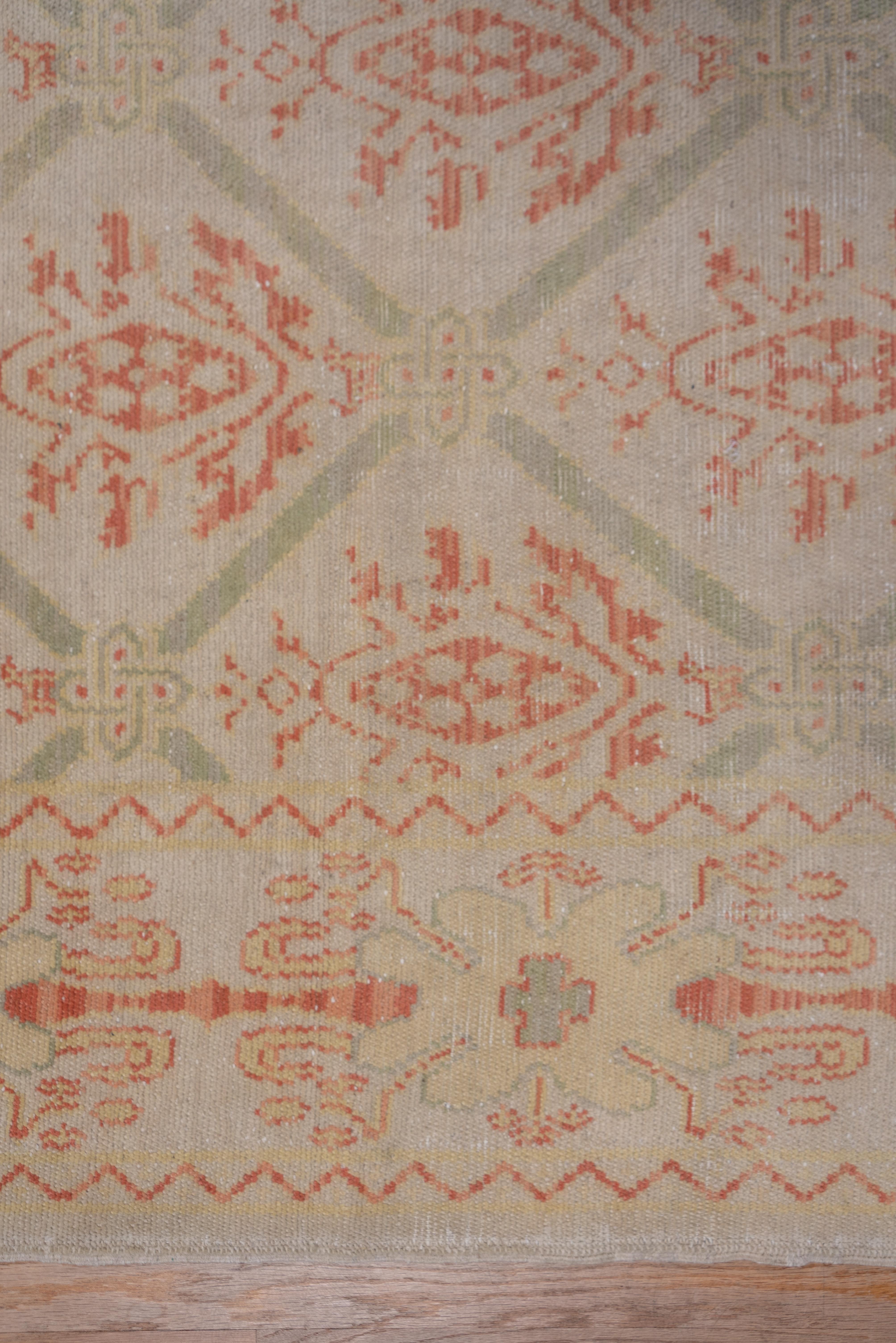 The sandy beige field shows an all-over one-way textile pattern of pomegranate palmettes enclosed by a lozenge lattice. Zig-zags mark out the main border with its knobby baton ornament. Rust is the most important detail tone.