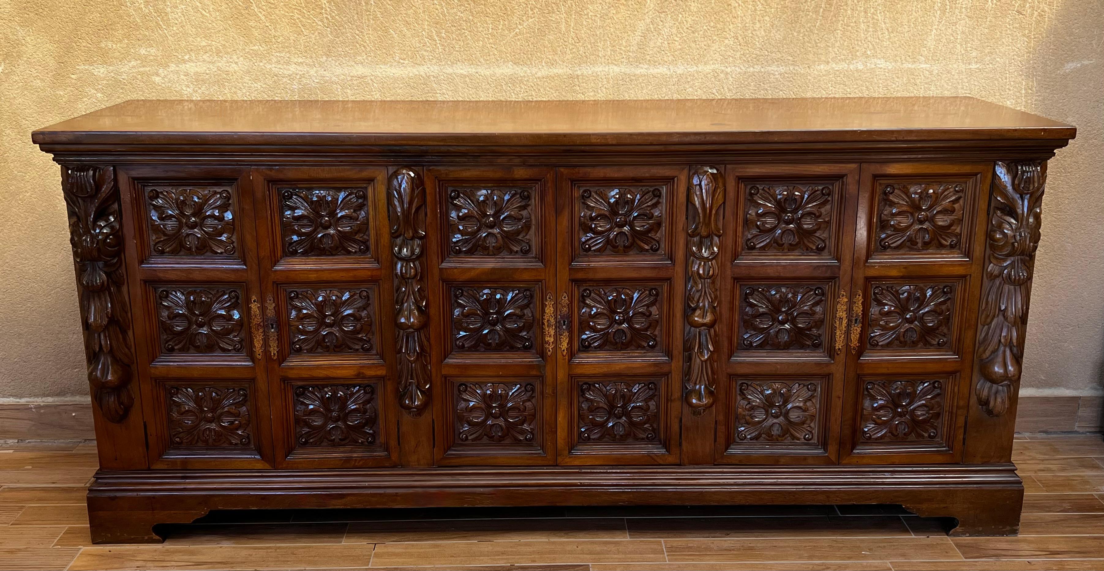 Diese stark geschnitzte Kredenz wurde um 1870 in Spanien hergestellt. Das Buffet ist aus massivem Nussbaumholz gefertigt und steht auf einem elegant verzierten Sockel. Der Schrank verfügt über sechs Türen auf der Vorderseite, die sich zu