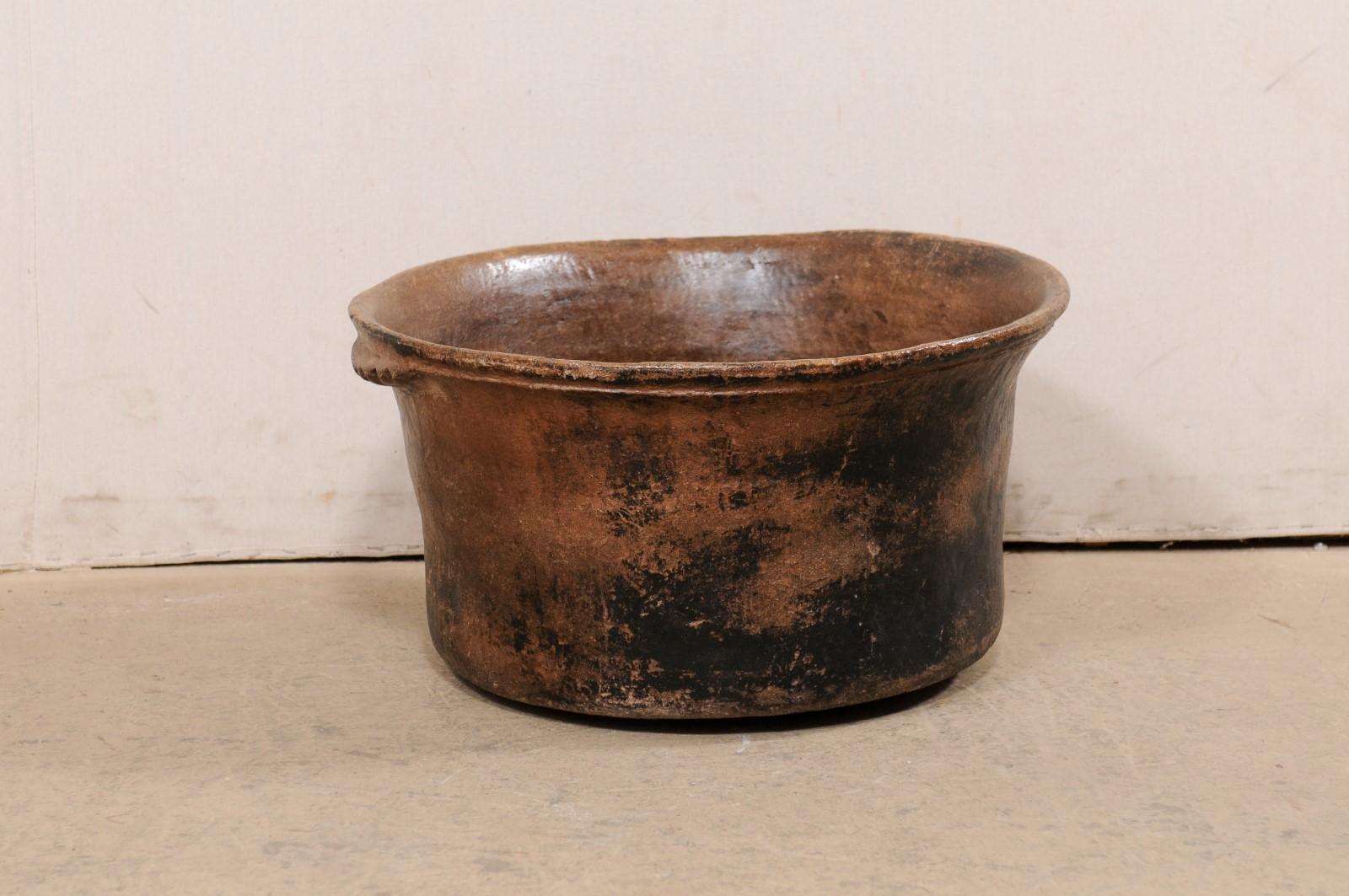 A Spanish Colonial cooking pot from the early 20th century, Central America. This antique cooking vessel has been made of clay, is round-shaped and flanked with two shallow handles with scalloped texture. The warm brown clay has a wonderful old