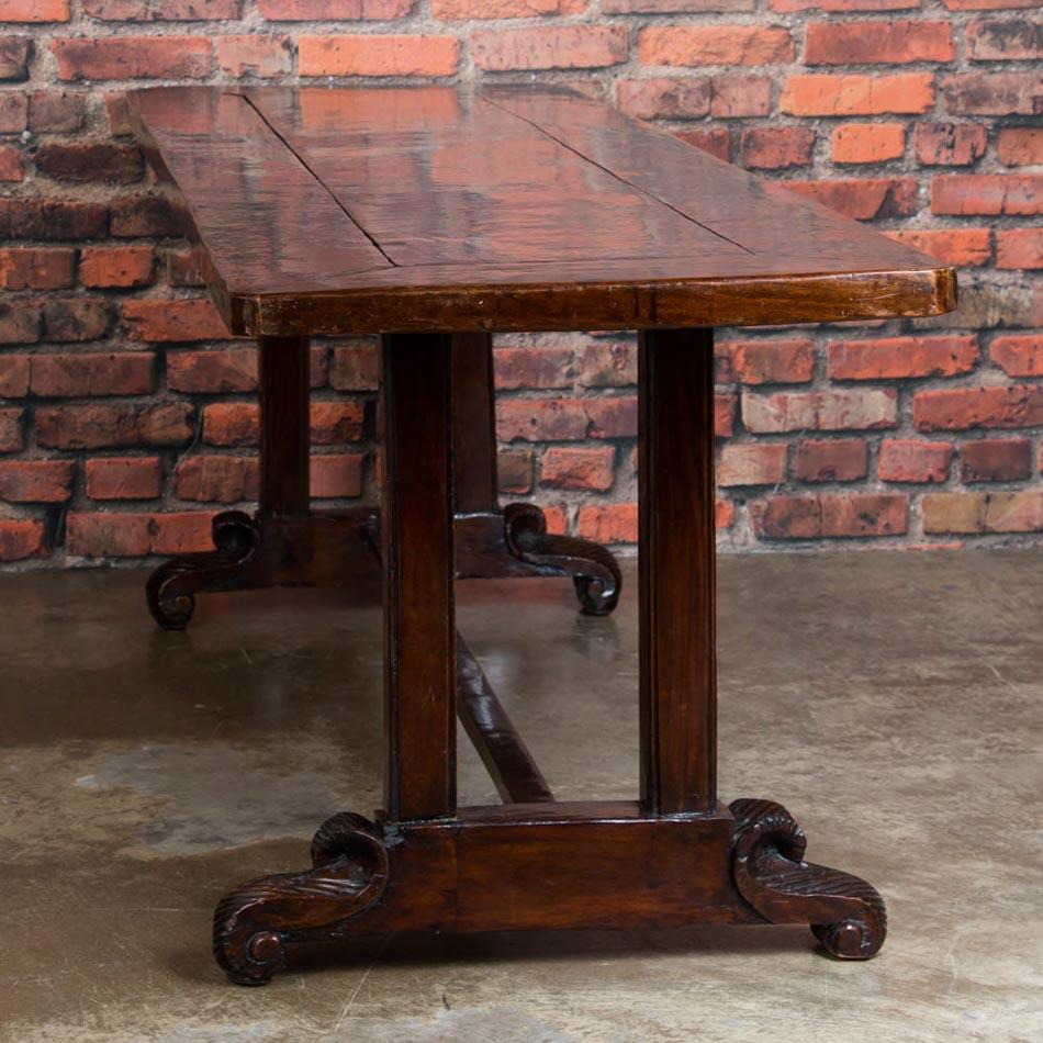 This long handcrafted dining table is stunning with it's dark hardwood top, sculpted legs and heavily carved scrolled feet. Made from a Philippine hardwood, the table has a light open feel with the hand carved legs and trestle base. The table has