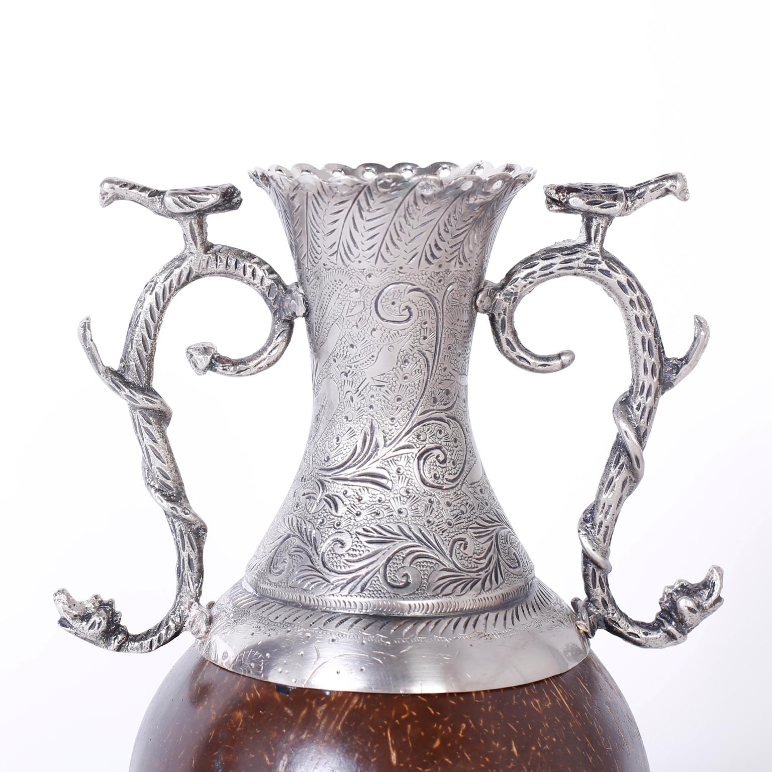 Vase antique de style colonial espagnol avec une combinaison inhabituelle de matériaux. Le vase est en métal argenté avec des gravures florales et des poignées gracieuses représentant des oiseaux sur des serpents. Le centre, à la manière
