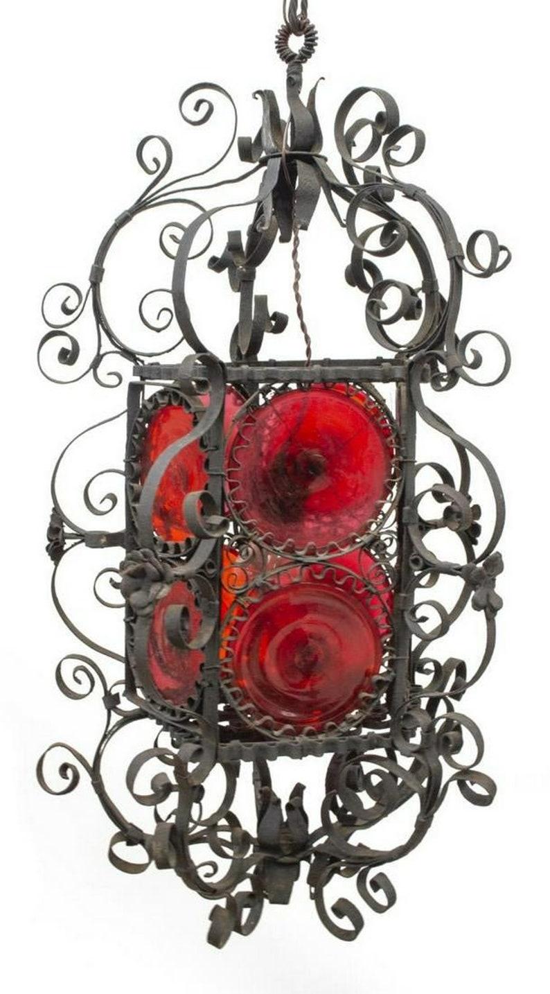 An impressive Spanish Revival hanging lantern from the early 20th century. Having a hand forged wrought iron frame decorated with ornate scrollwork and floral, ten hand blown red bullseye glass, having a hinged door opening to single hanging light.