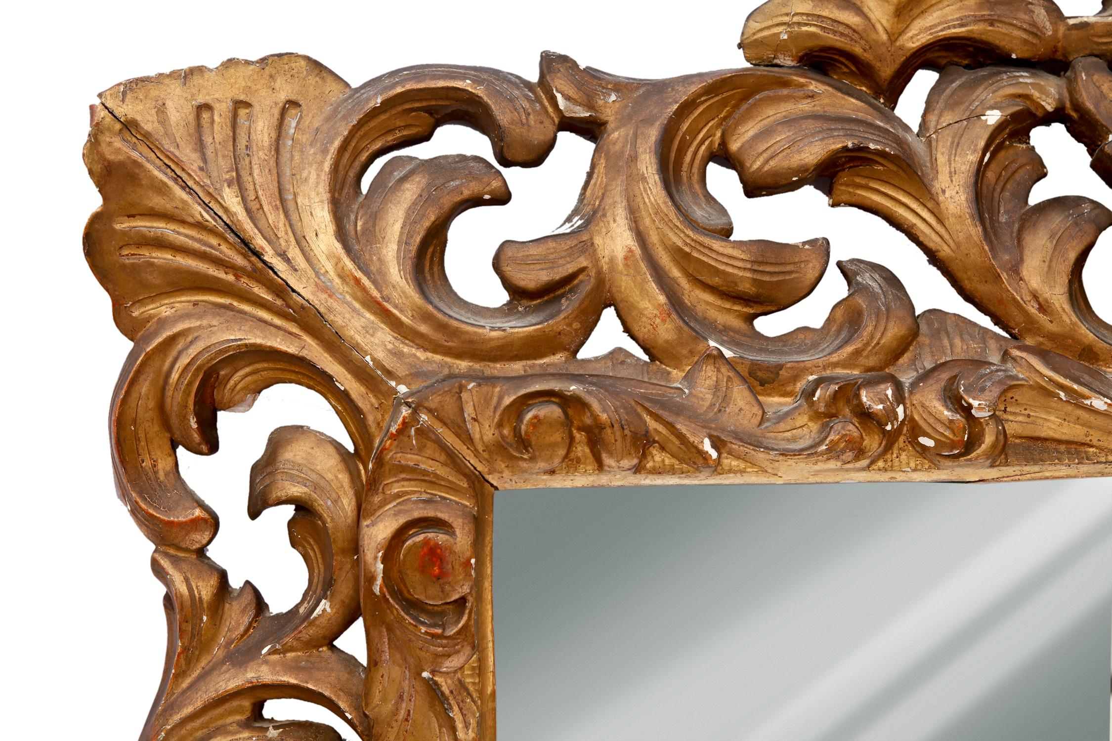 This ornately carved mirror is a fabulous focal point to any room. Boldly carved scrolls and leaves are heavily gilded with a beautiful patina. In some places a dark red ochre underpainting is revealed which adds to the depth and interest of the