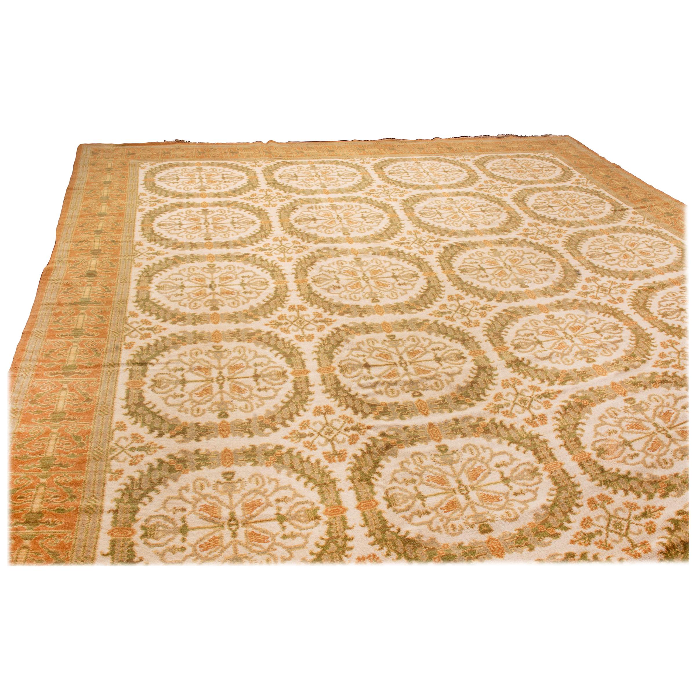 Originating from Spain in 1920, this antique traditional wool rug from Rug & Kilim employs an ornate series of kaleidoscopic floral medallions throughout the beige and greenfield design. Hand knotted in durable wool, the border wraps continuously